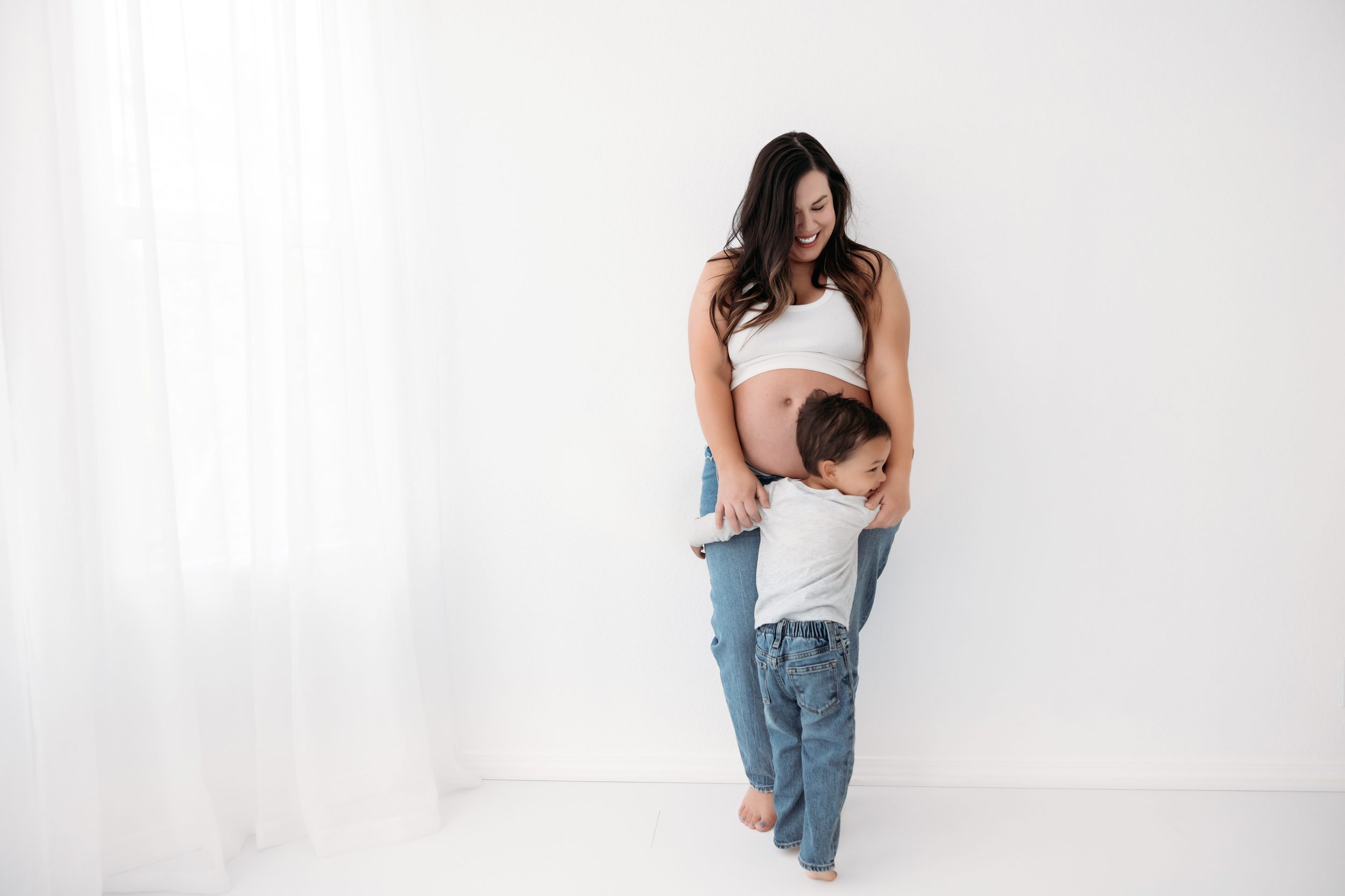 Pregnant mom and toddler boy snuggling her belly