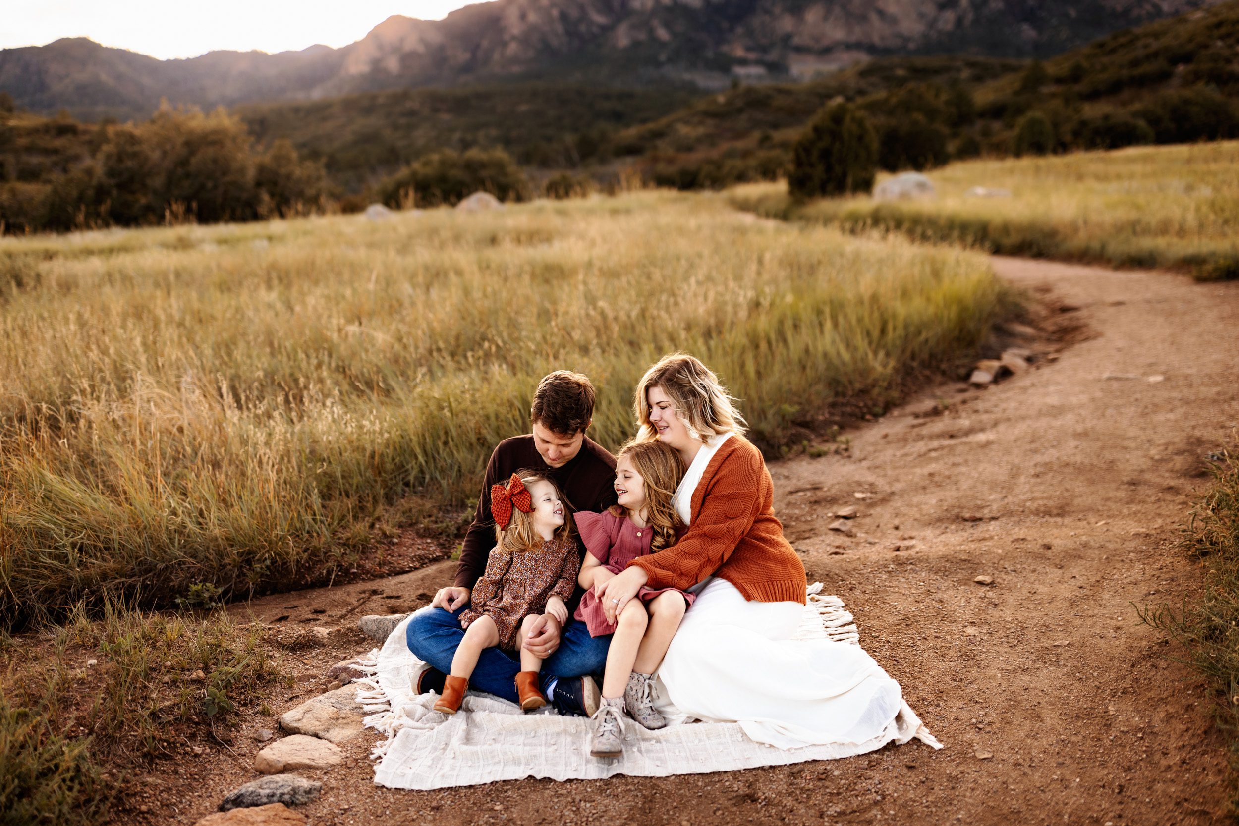 Family sitting on a white blanket together with the mountains behind them