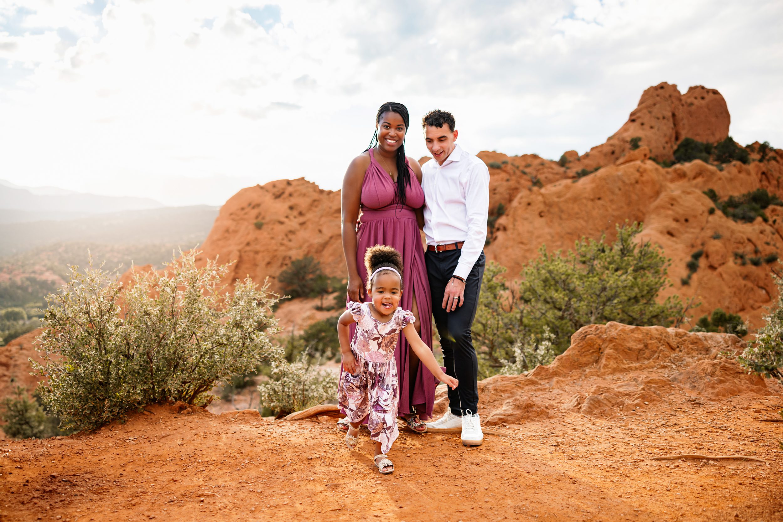 Family standing together on red rocks at Garden of the Gods with dramatic rock formations and soft evening light