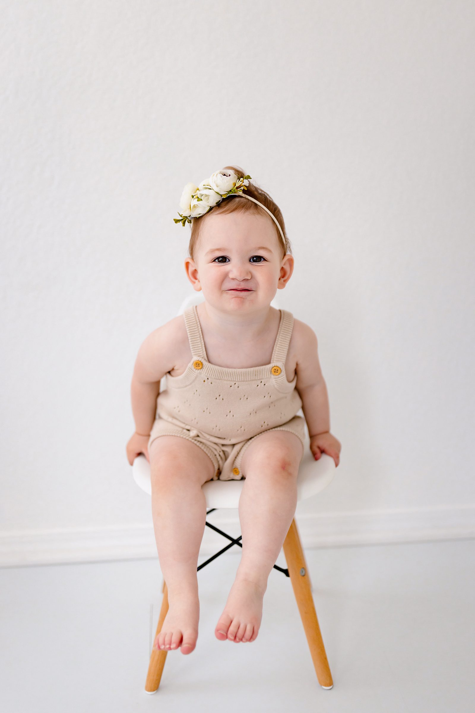 One-year-old sitting on a small stool in a neutral outfit, smiling in a clean white studio setup