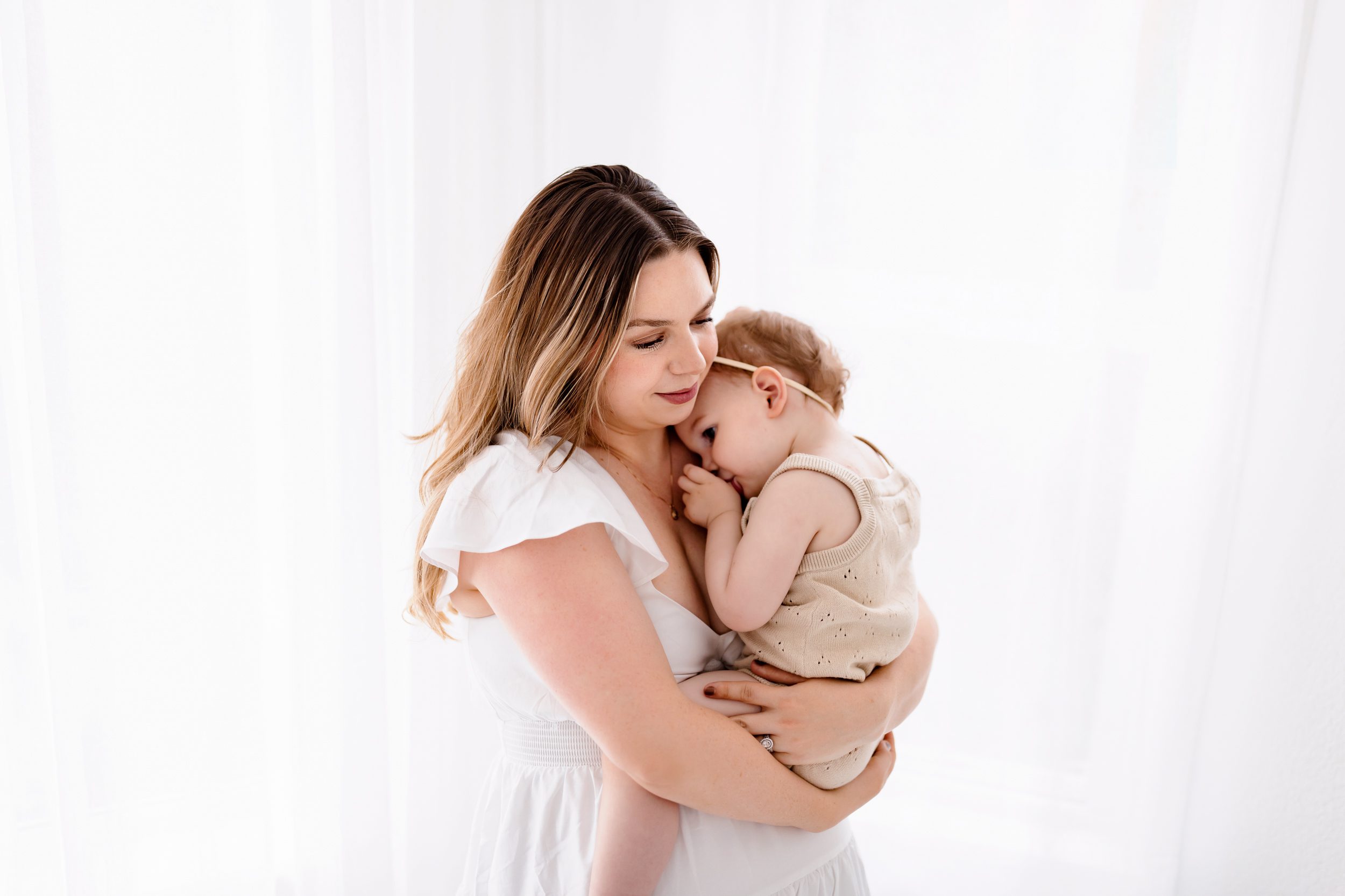 Mother gently cuddling her toddler who is resting against her shoulder in a soft, light-filled studio