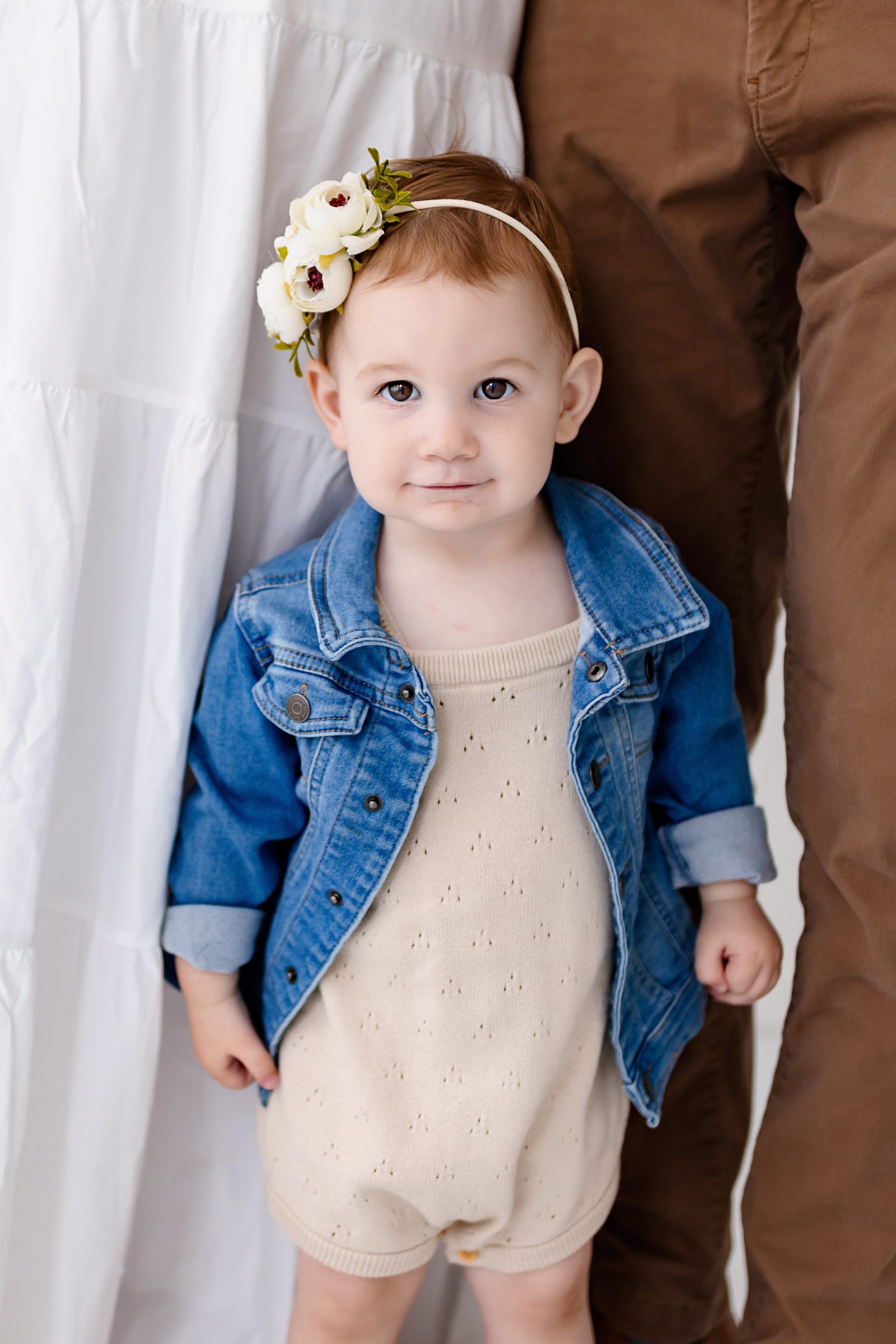 One Year milestone photos in Colorado Springs of a toddler standing in a neutral studio wearing a cream romper and denim jacket