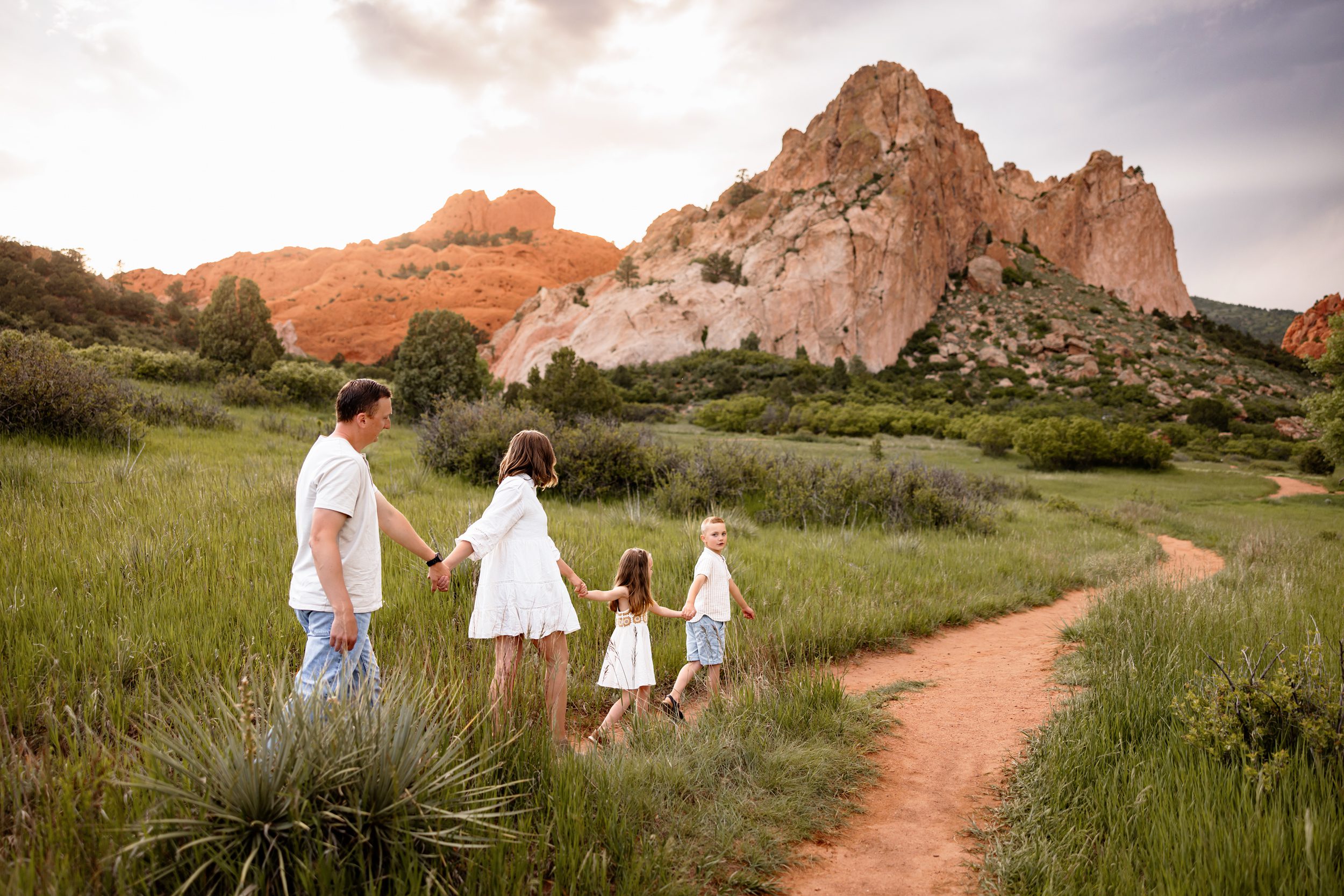 Family walking away together on a dirt trail with red rocks and soft sunset light in Colorado