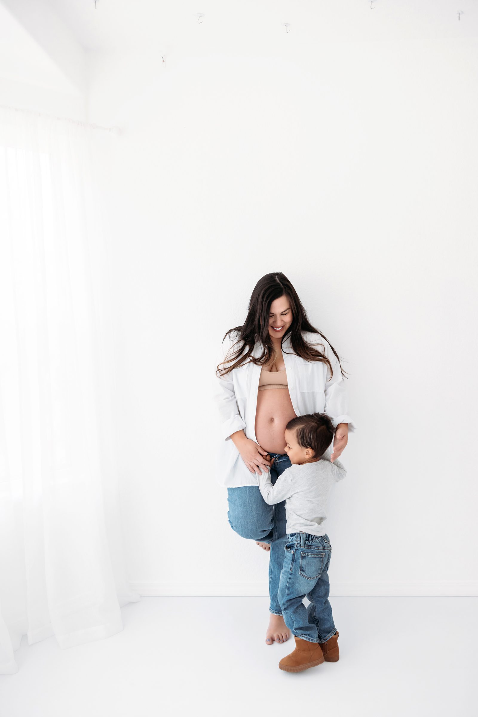 indoor photo of pregnant mom and toddler hugging her belly