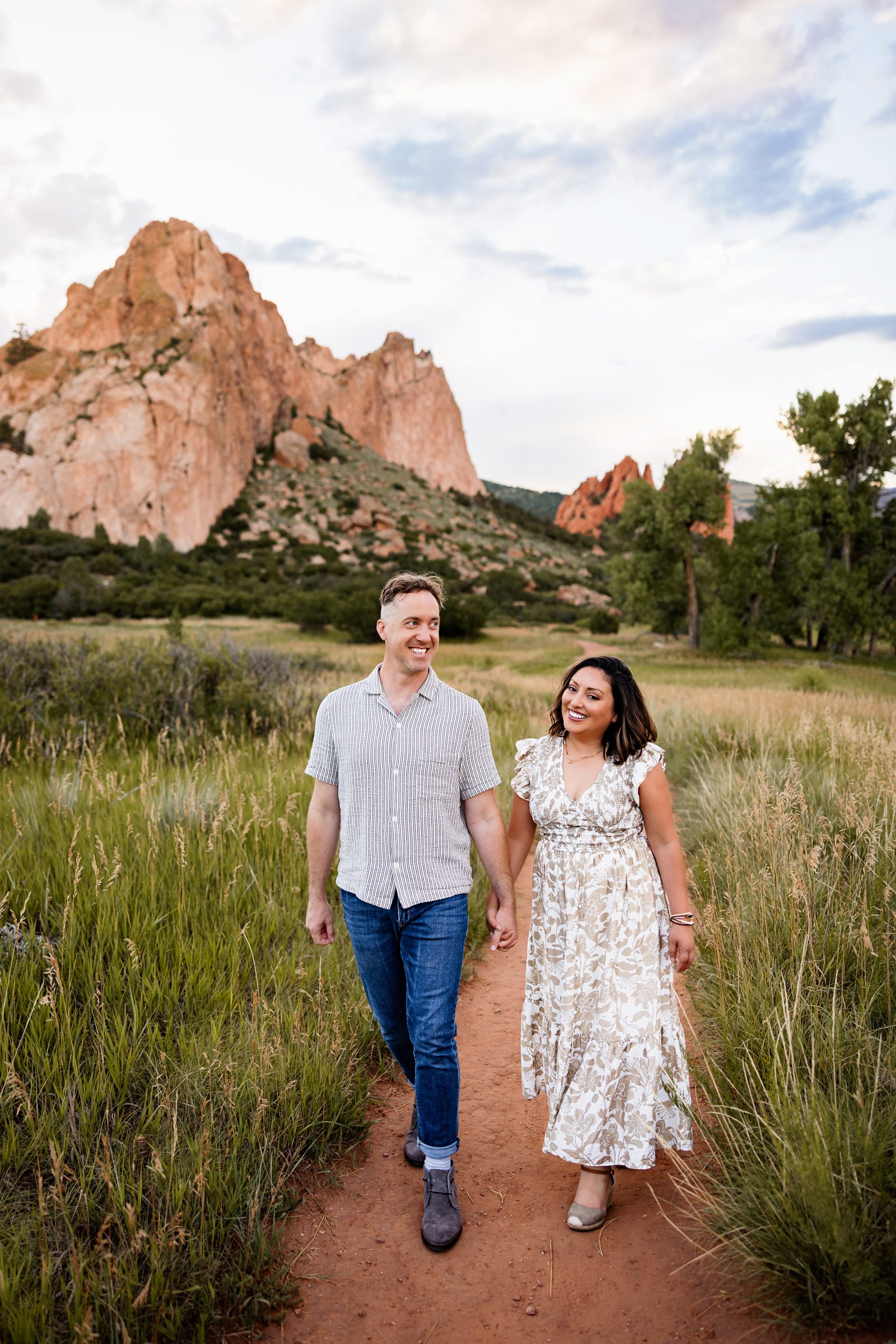 Summer Family Photos in Colorado Springs of a couple walking along a trail surrounded by tall grass and mountain views
