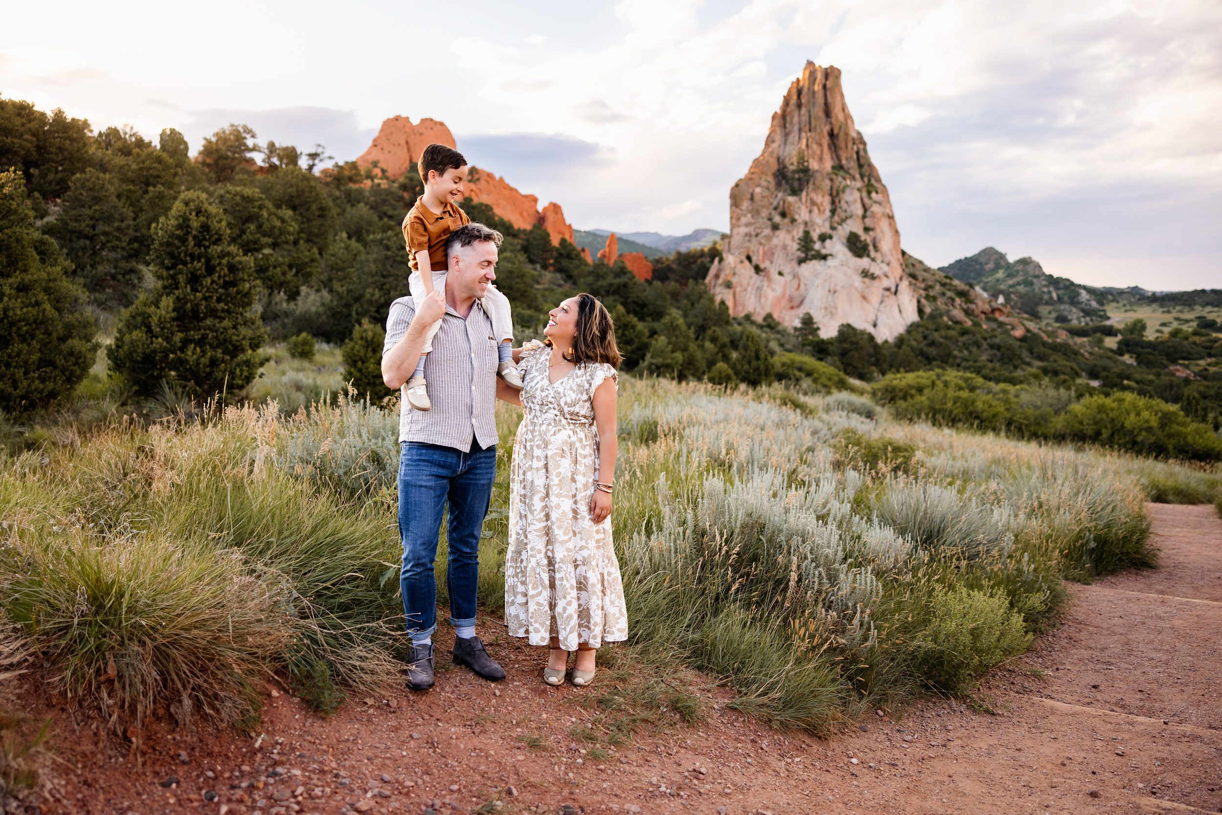 Summer Family Photos in Colorado Springs at Garden of the Gods with parents and child smiling together along a trail with red rock formations and mountain views