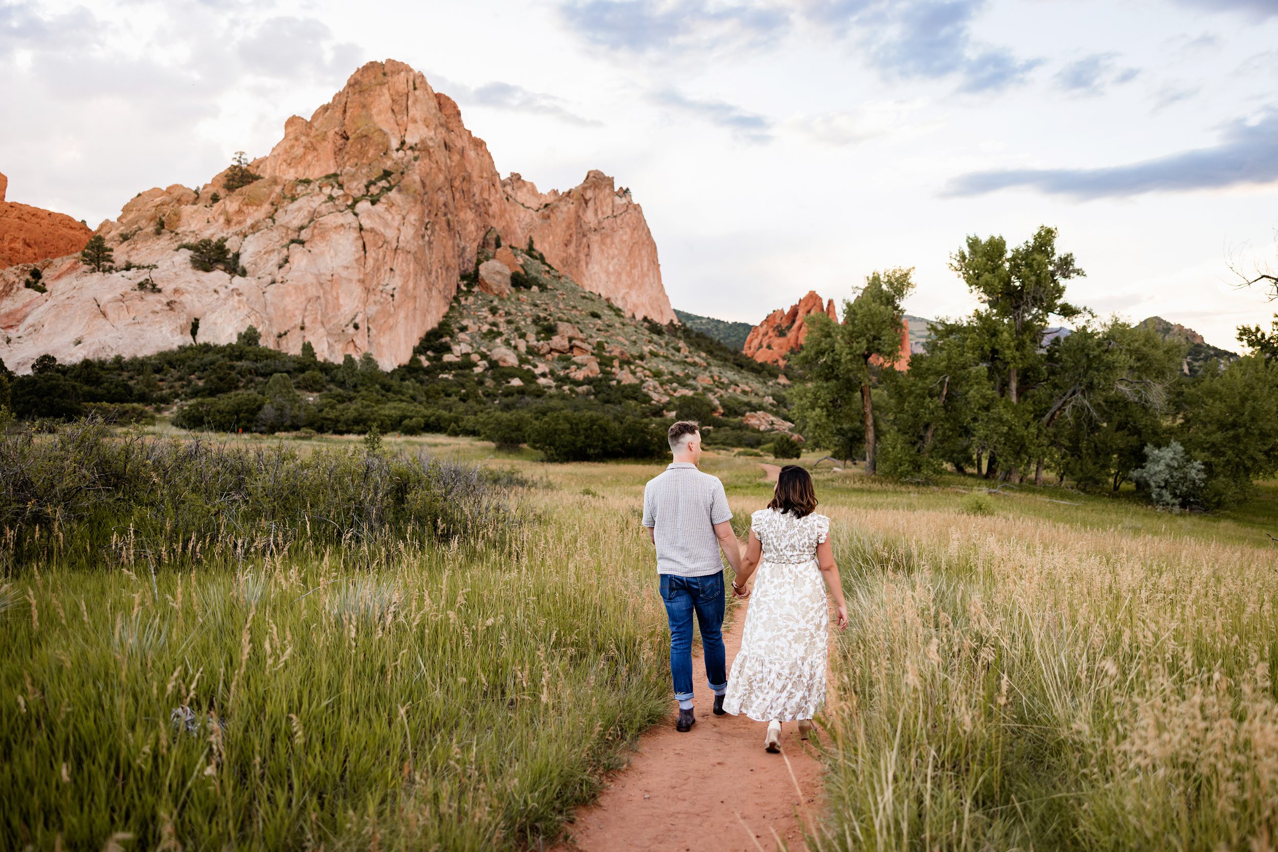 Couple walking away together on a dirt path through a meadow with red rock formations and mountain views