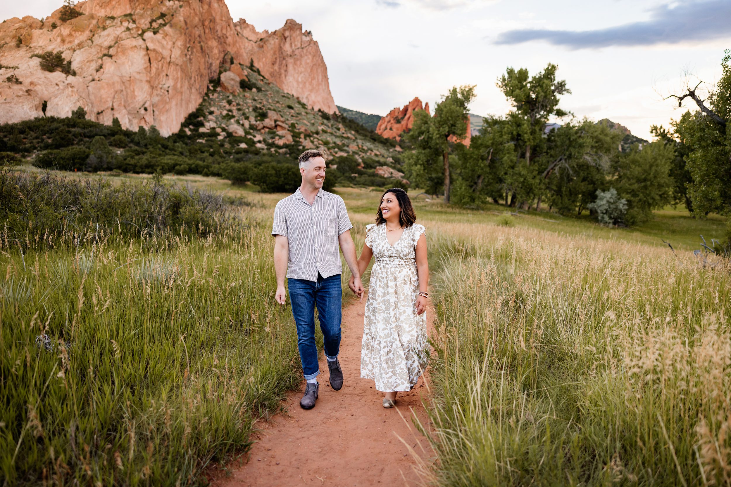 Summer Family Photos in Colorado Springs at Garden of the Gods with a couple walking hand in hand on a trail through tall grass