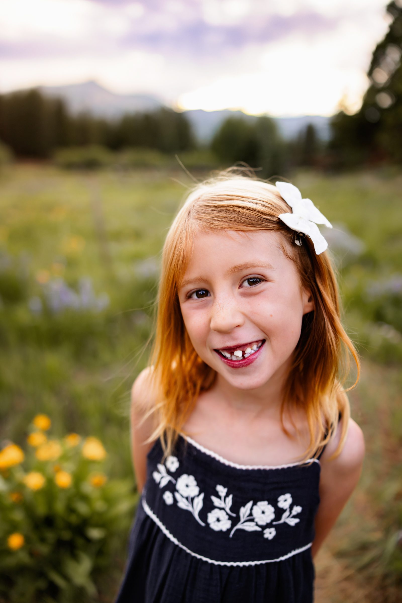 Smiling little girl with a white bow during a golden hour family session in the mountains