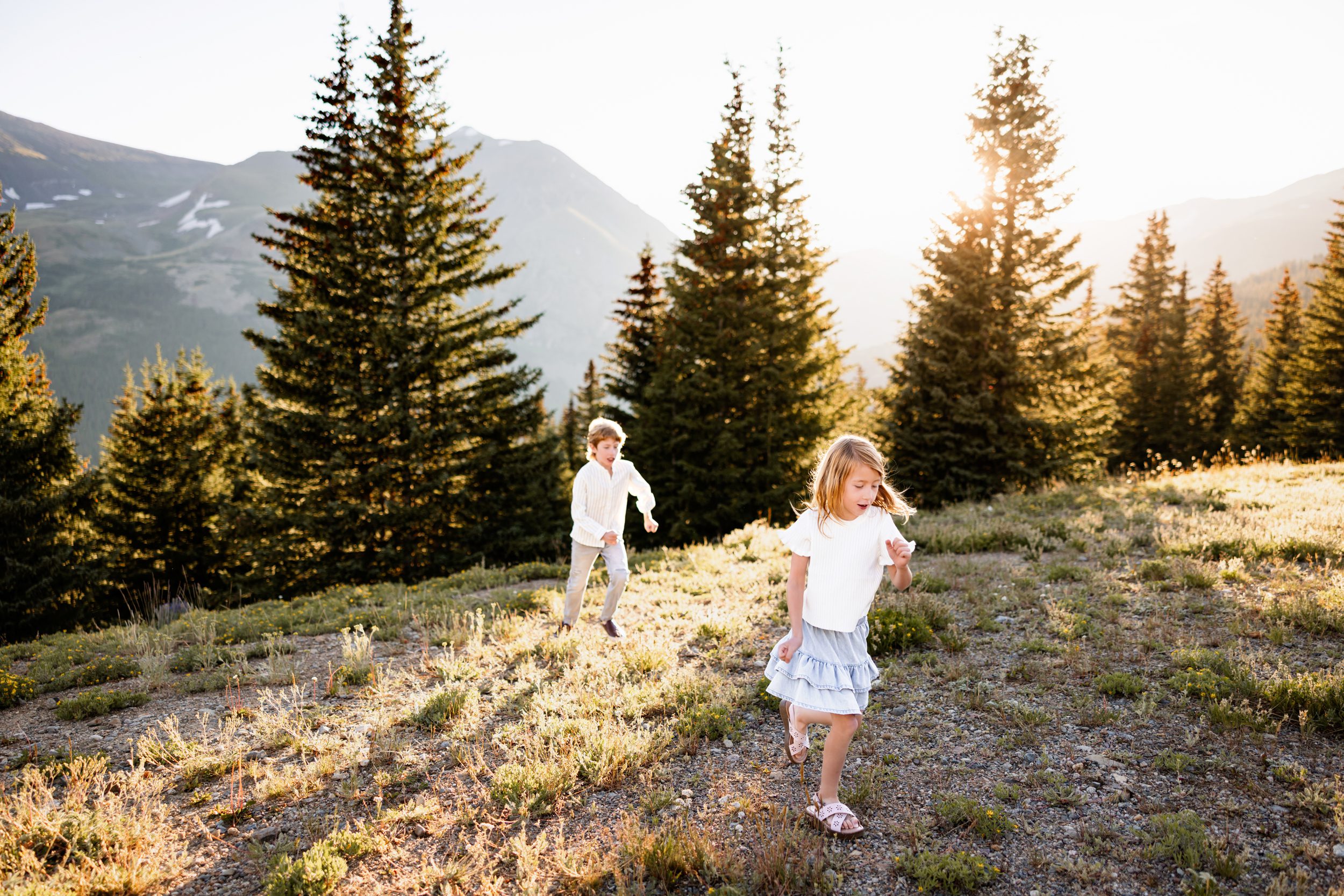 Breckenridge Family Photographer capturing playful siblings running through a glowing mountain field at sunset