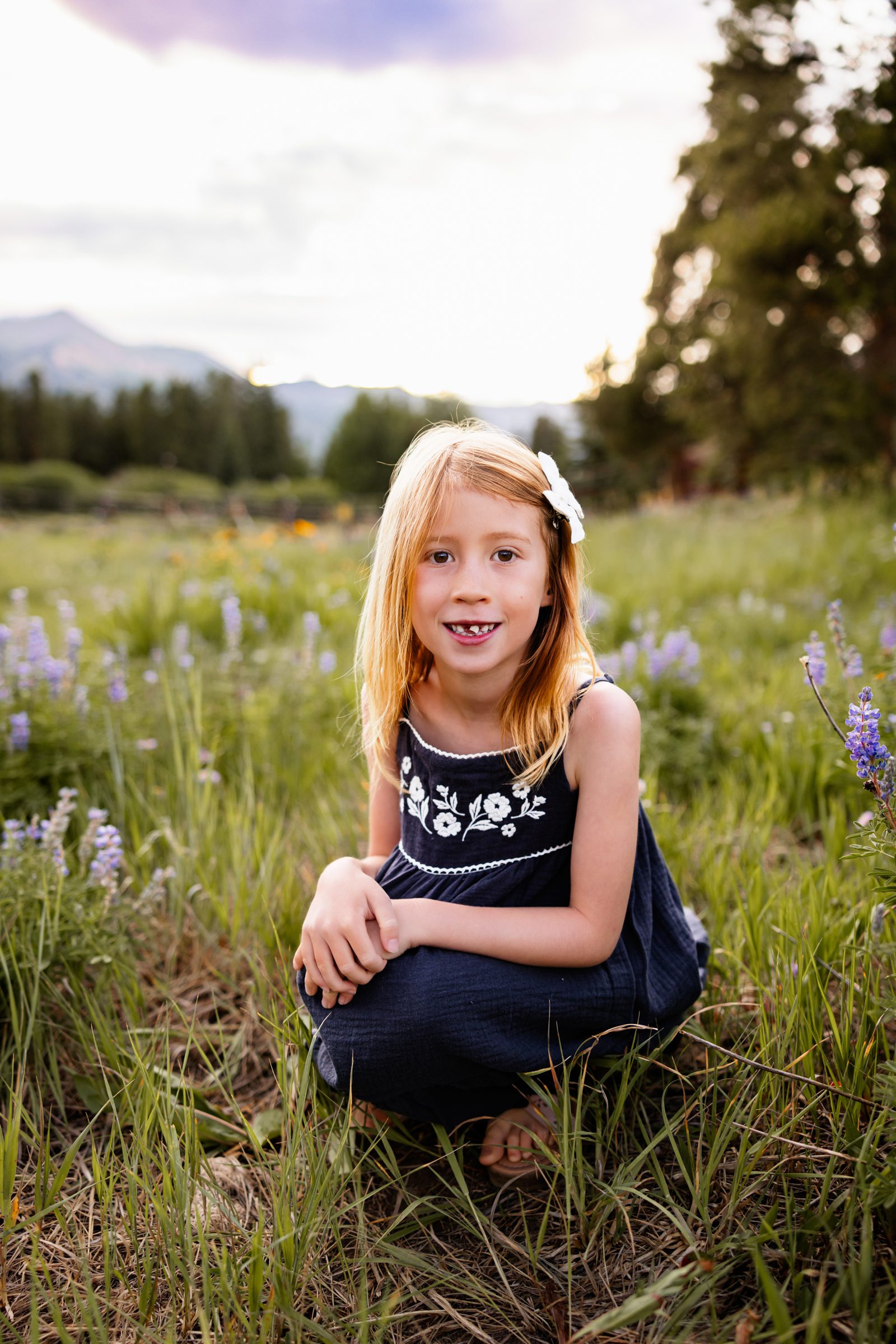 Close up portrait of a young girl sitting in a Breckenridge wildflower meadow with mountains and soft evening light in the background