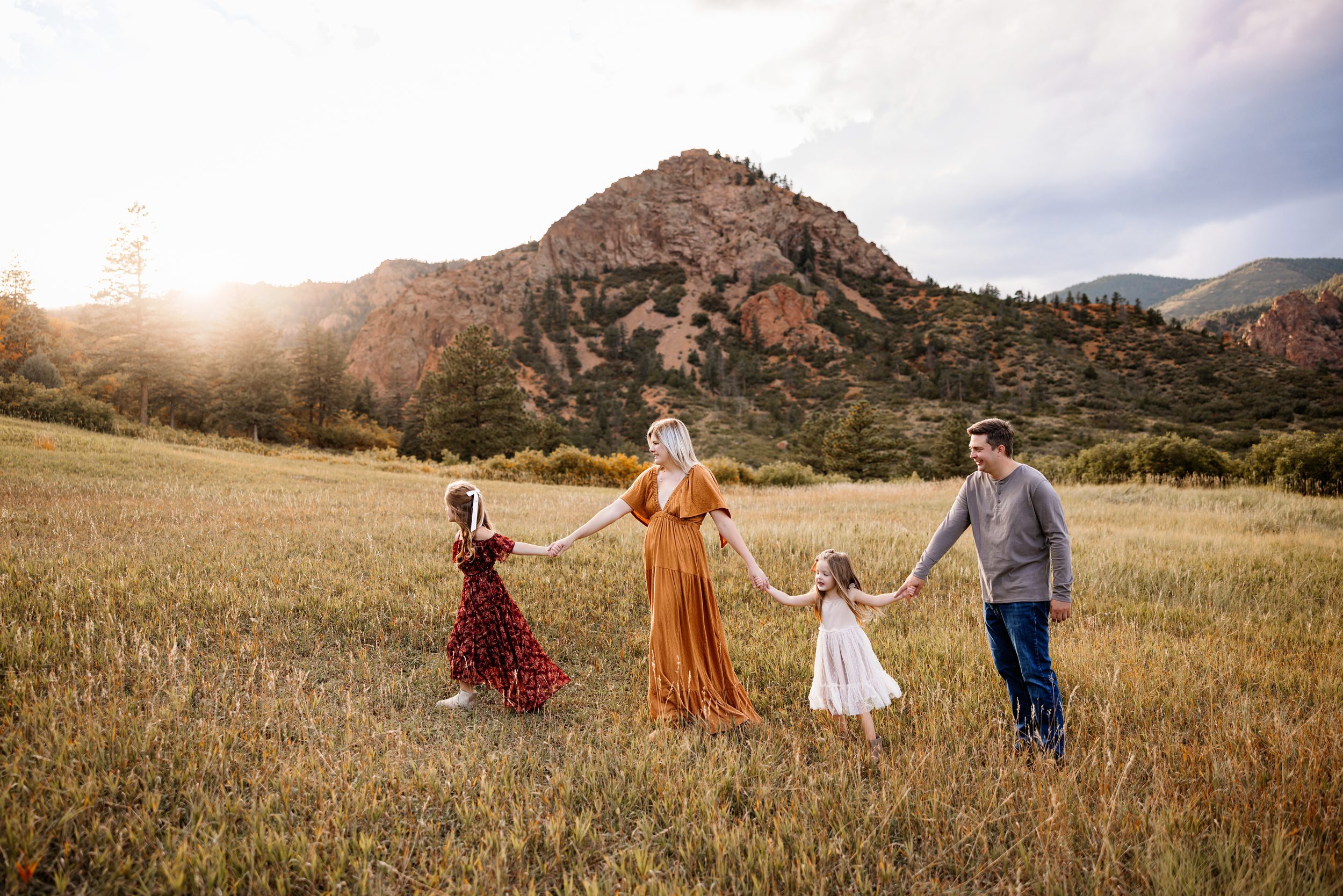Candid Fall Family Photos Colorado Springs capturing a family holding hands and walking through a golden meadow with mountain views and soft evening light