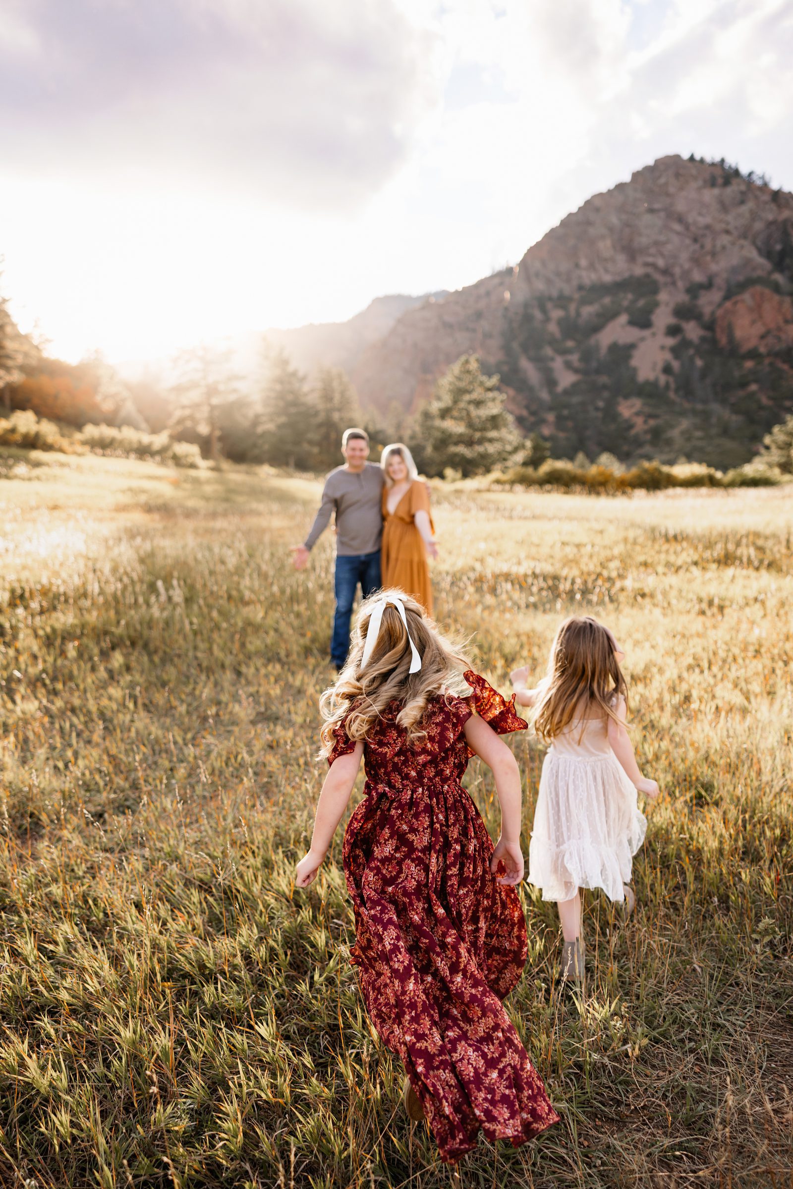 two young girls running through a sunlit field toward their parents with mountains glowing in the background