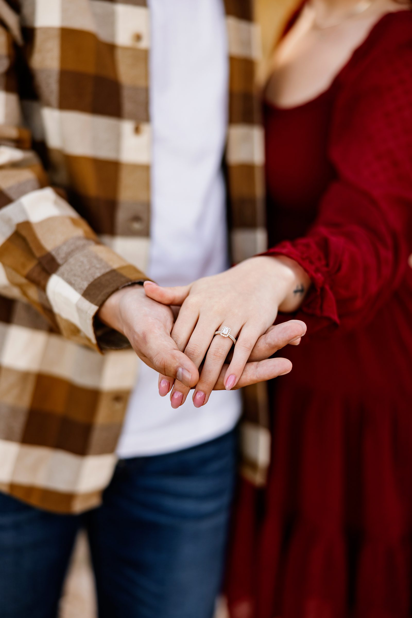Detail of engagement ring while couple holds hands 