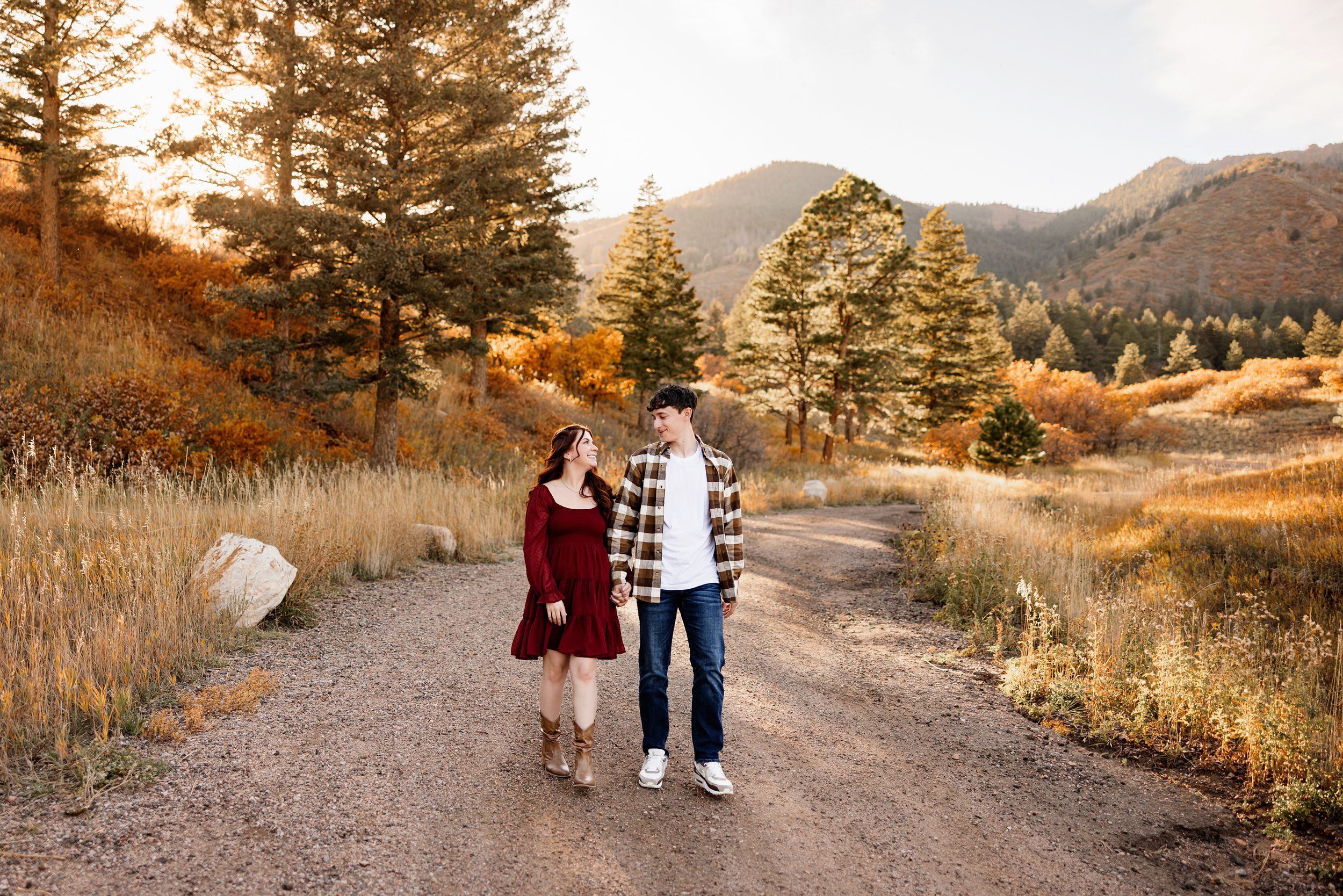 Couple walking hand in hand on a dirt road with golden light and fall trees in Colorado Springs