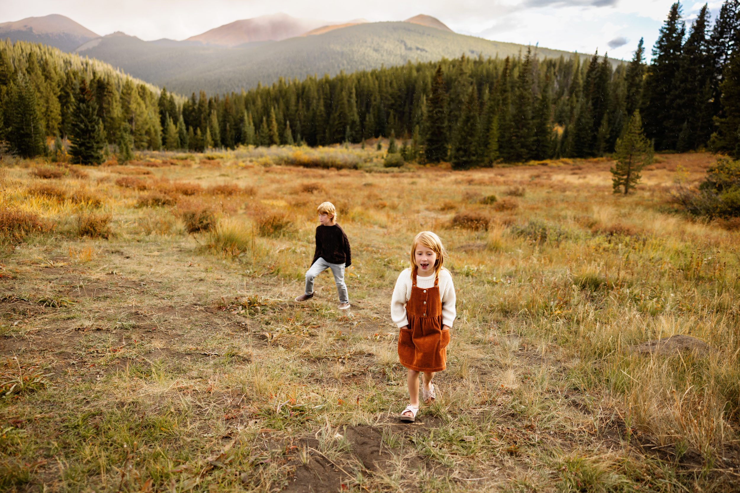 Fall Family Photos in Breckenridge capturing siblings walking through a wide alpine field with mountain views
