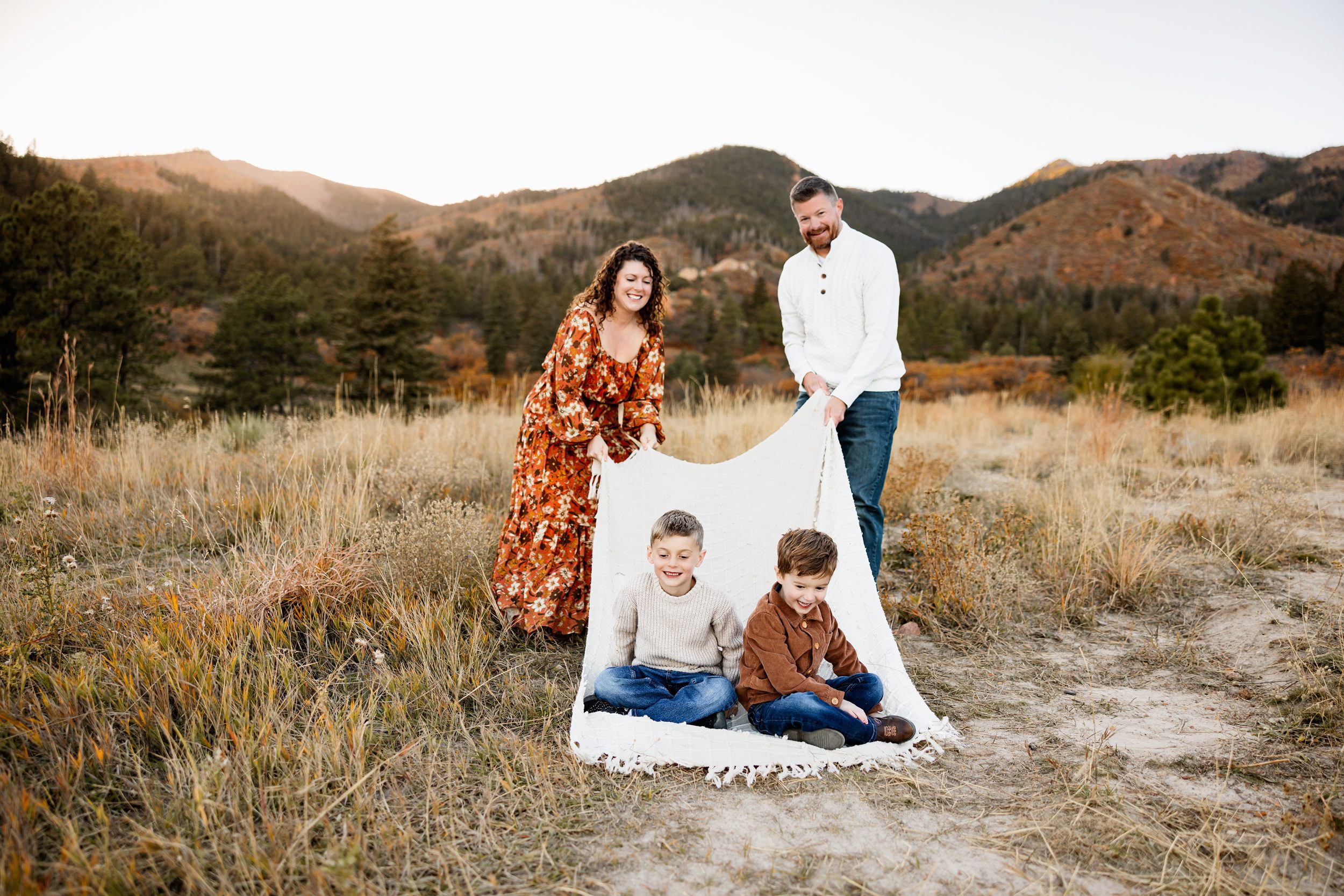 Parents holding a blanket while kids sit and laugh during a playful outdoor fall family session