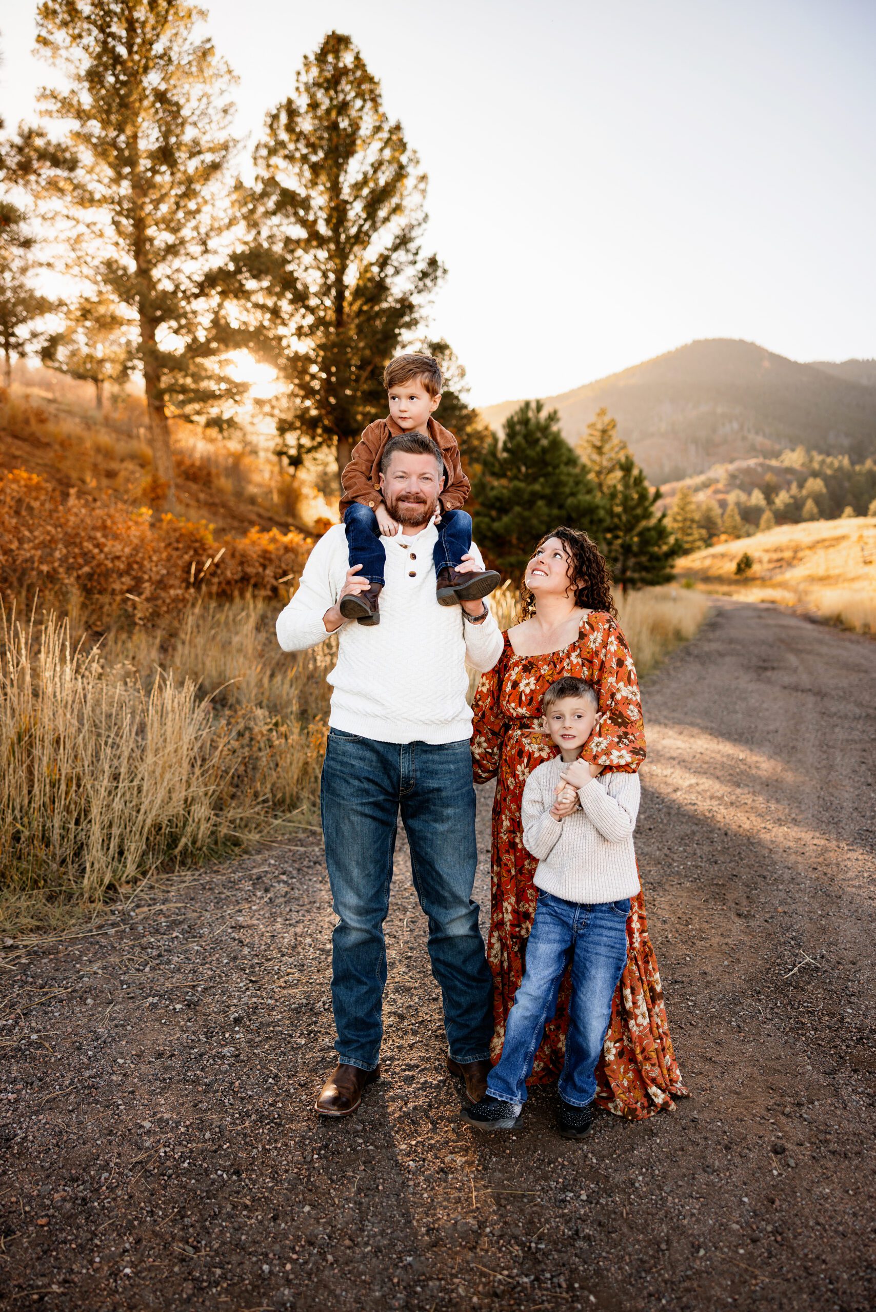 Dad holding child on shoulders while mom and sibling stand close during sunset family photo session