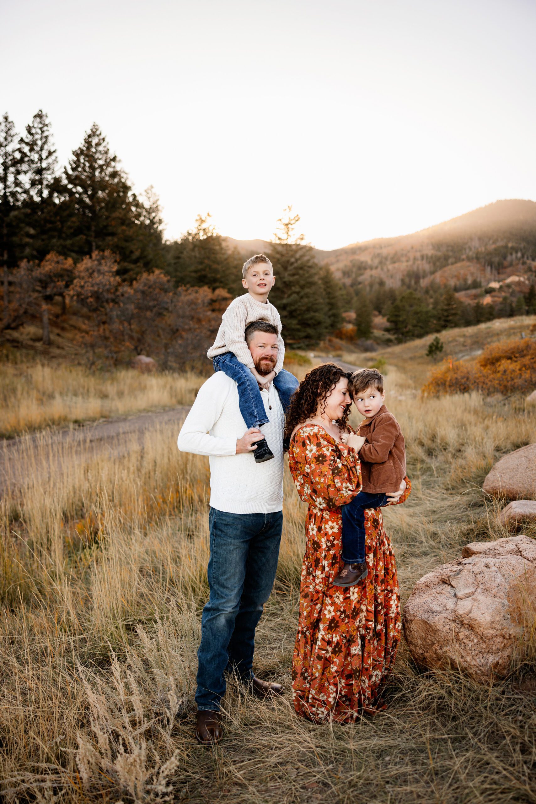 Family standing together in a mountain meadow with warm fall colors and soft sunset light