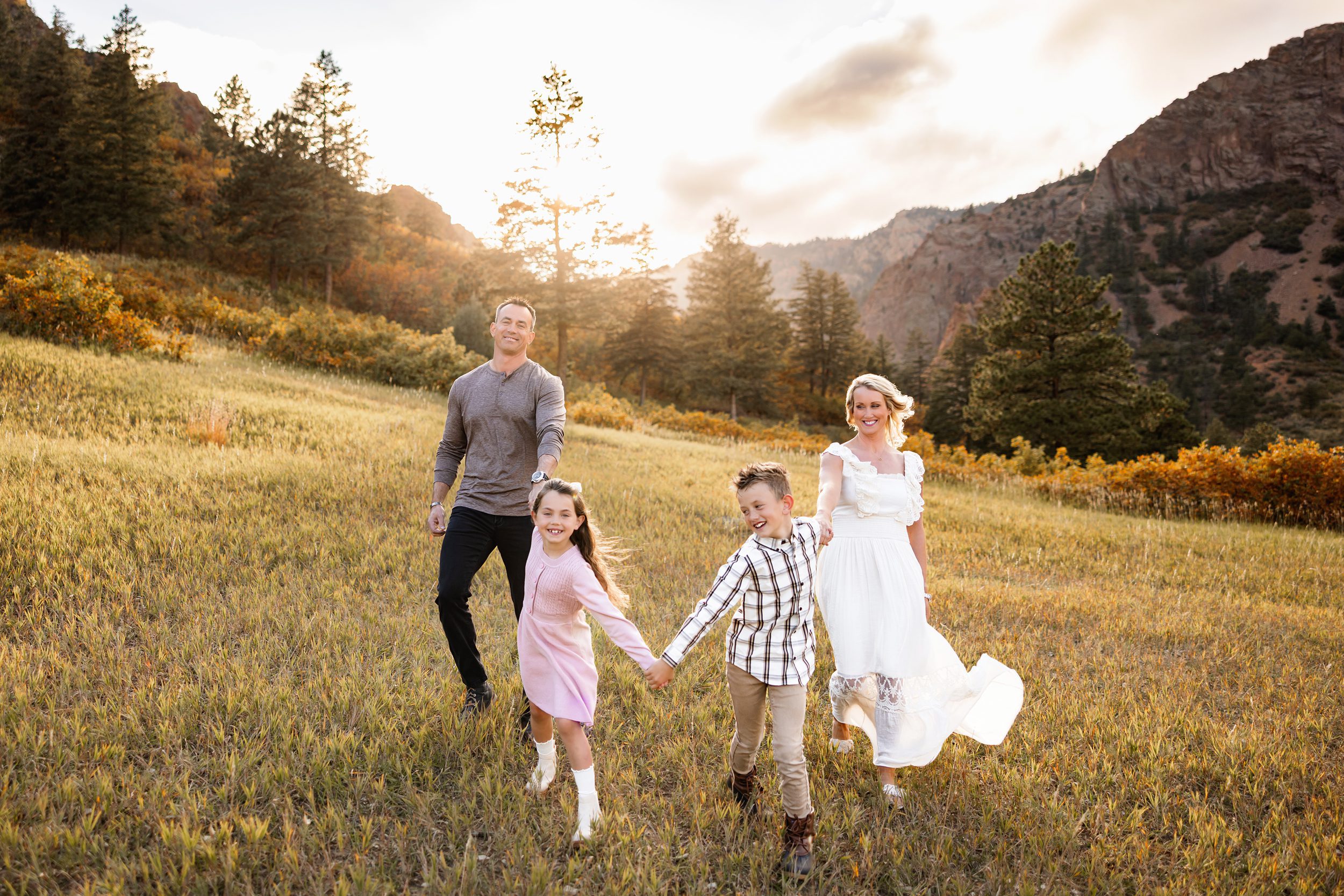 Family of four running together through an open field with mountains and golden light in the background