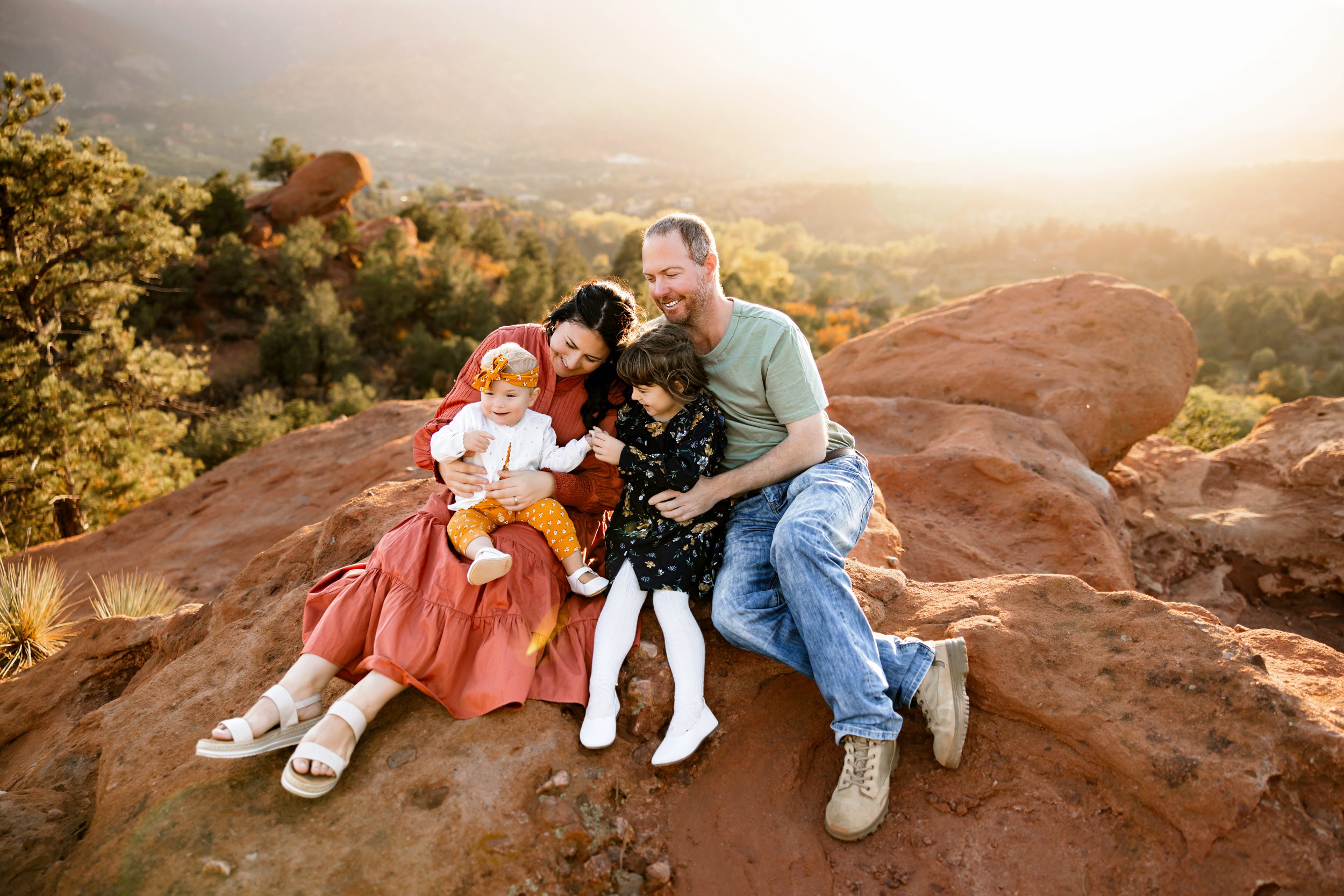 Garden of the Gods family photos of a family sitting on red rocks at golden hour, sharing candid smiles and playful moments with their young children