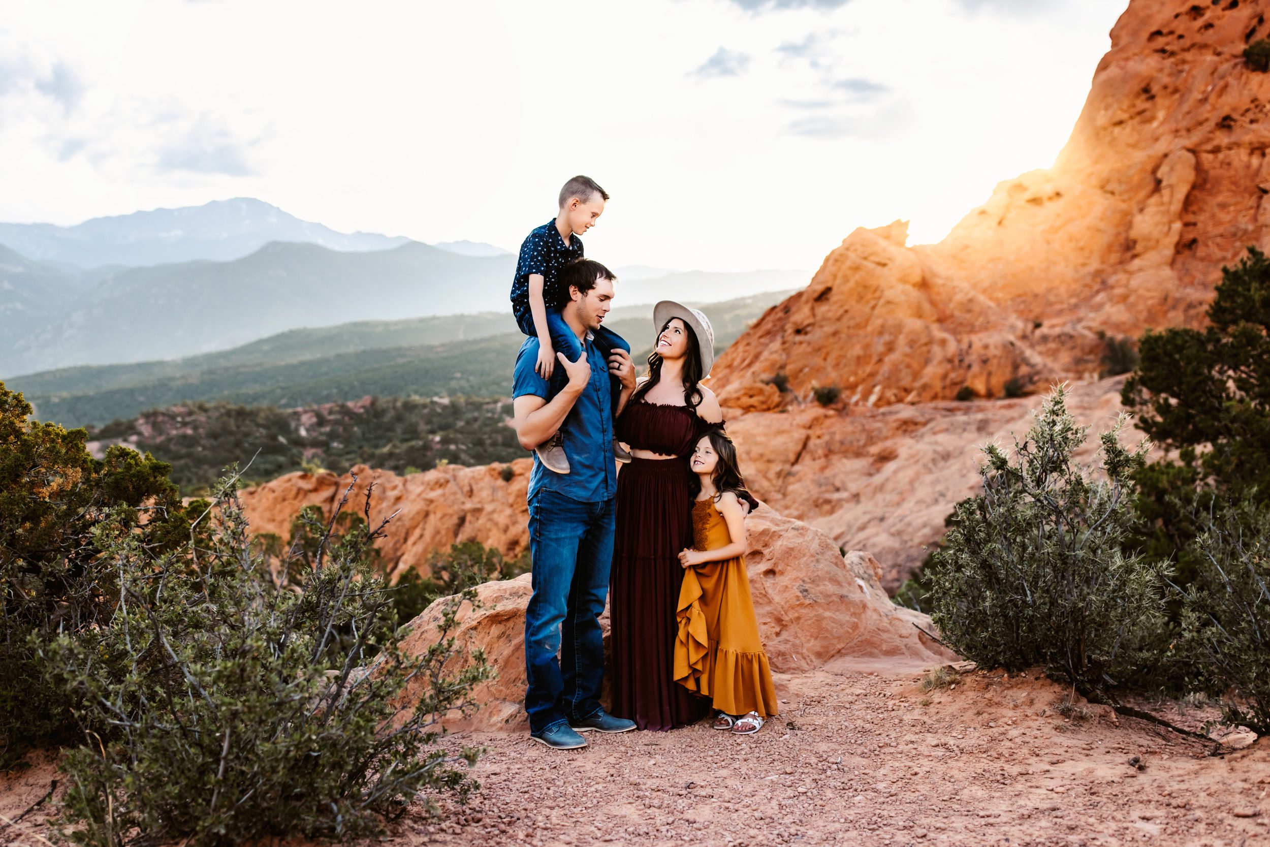 Garden of the Gods family photos with a family of four standing together on red rocks at sunset with mountain views in Colorado Springs