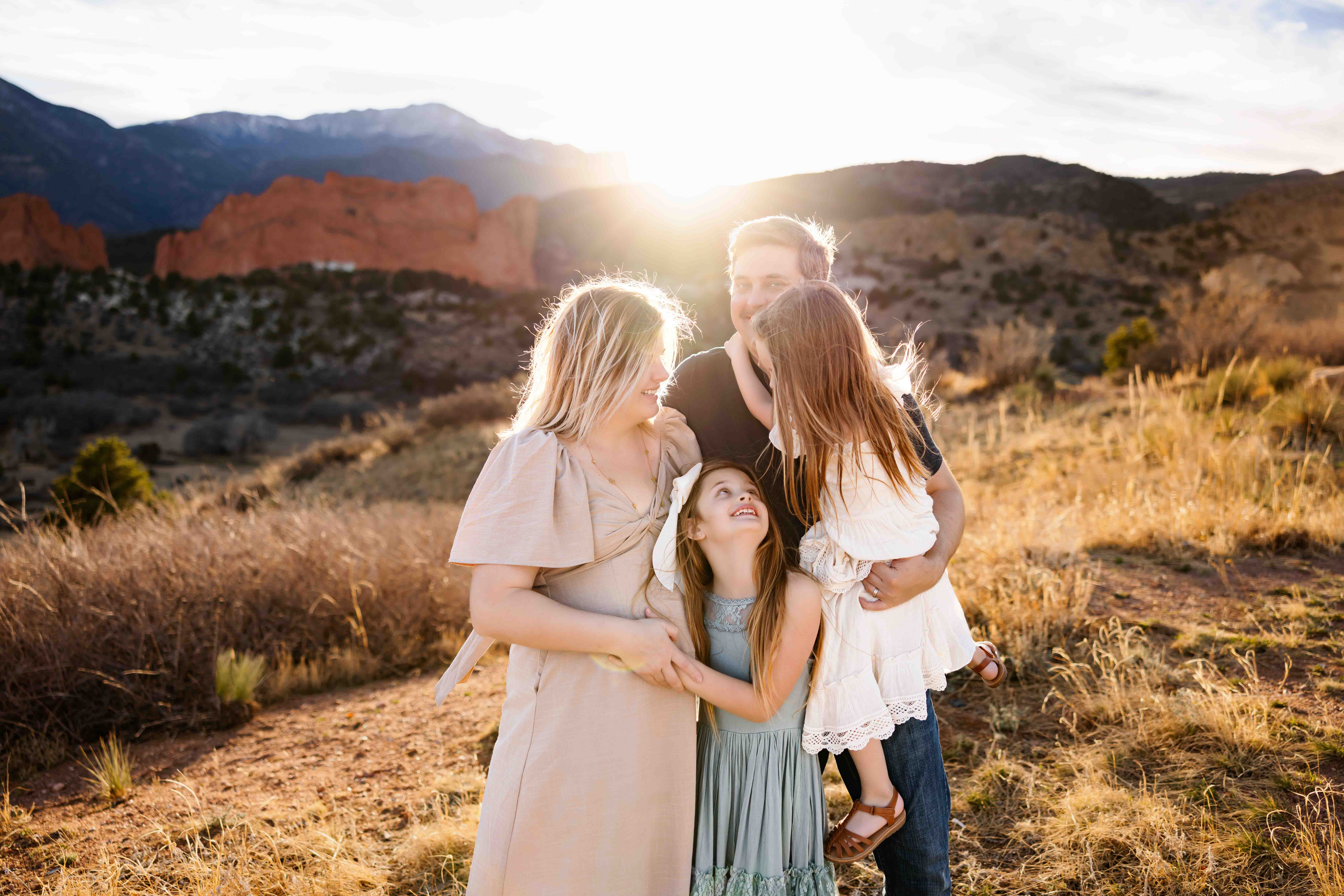 Family hugging and laughing together in a grassy field with red rock formations and glowing sunset light