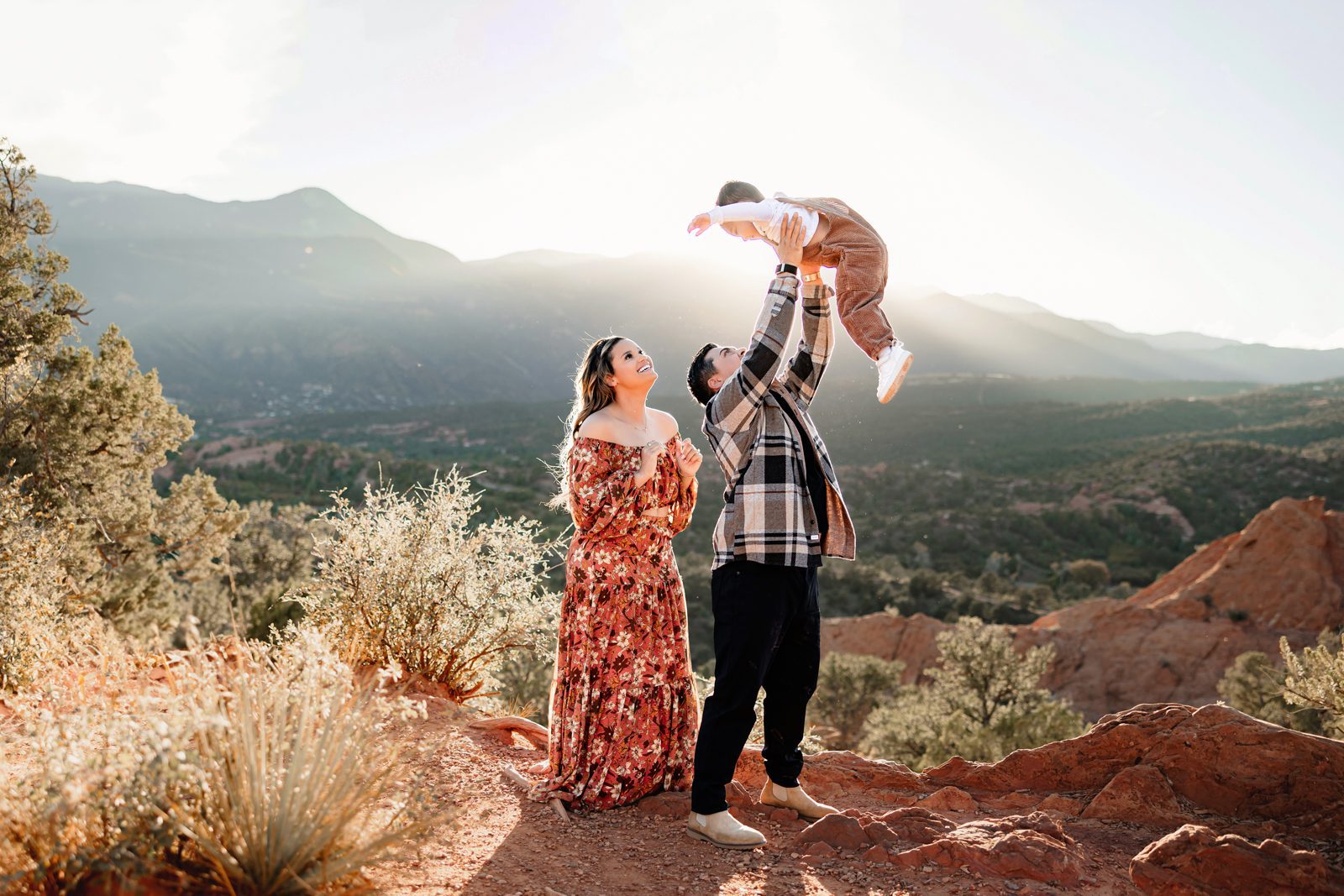 Garden of the Gods Mini Session dad lifting toddler into the air with mountains and sunset light