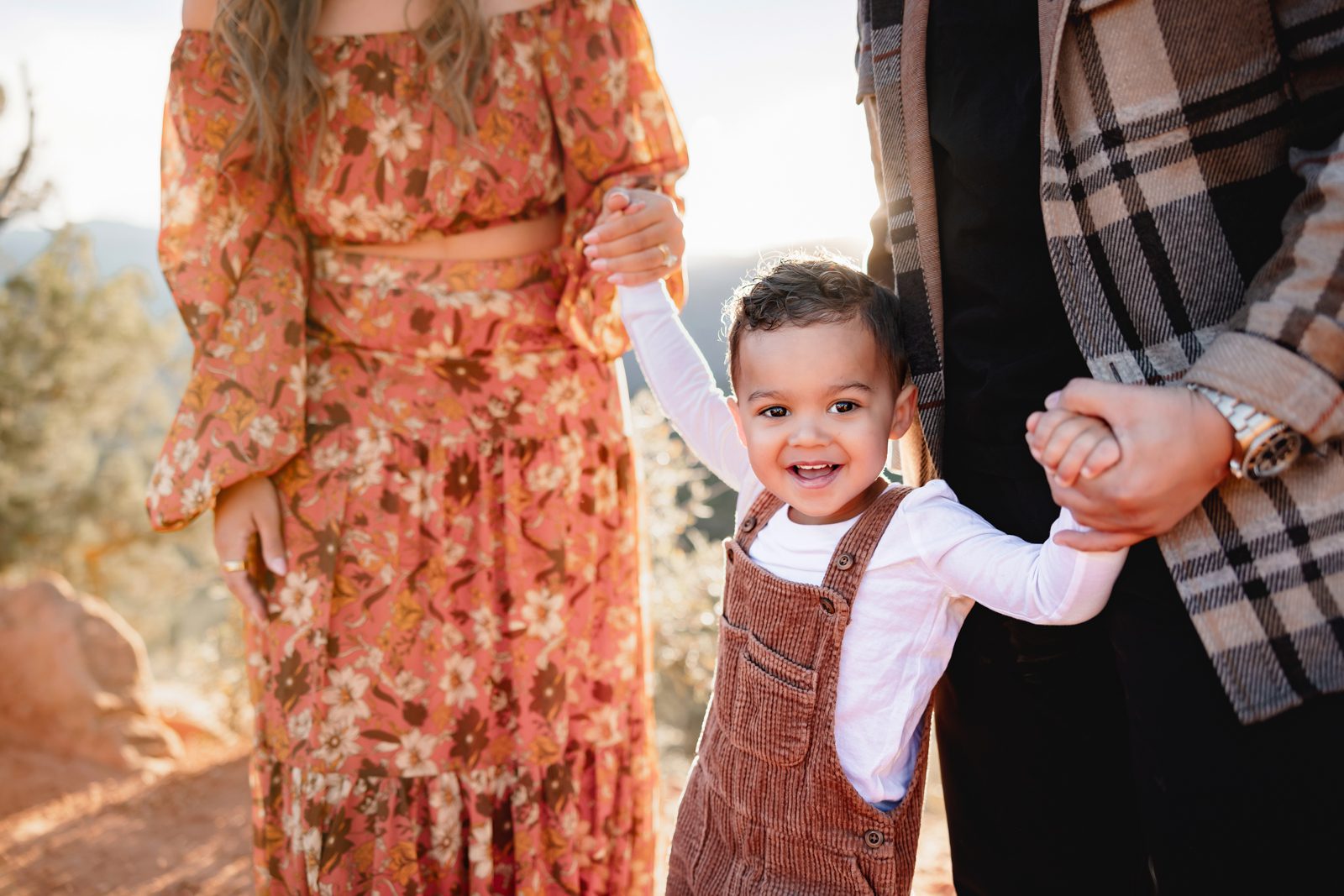 Parents helping toddler walk along a scenic trail with soft sunset light in Colorado Springs