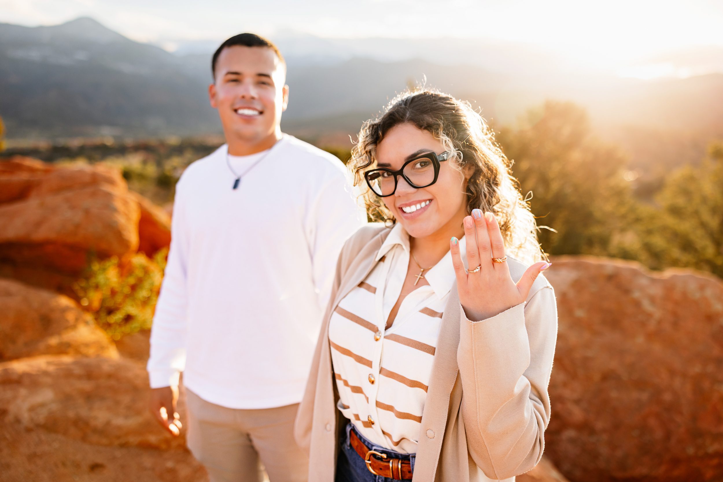 Woman showing off engagement ring with partner smiling in the background at Garden of the Gods proposal photos