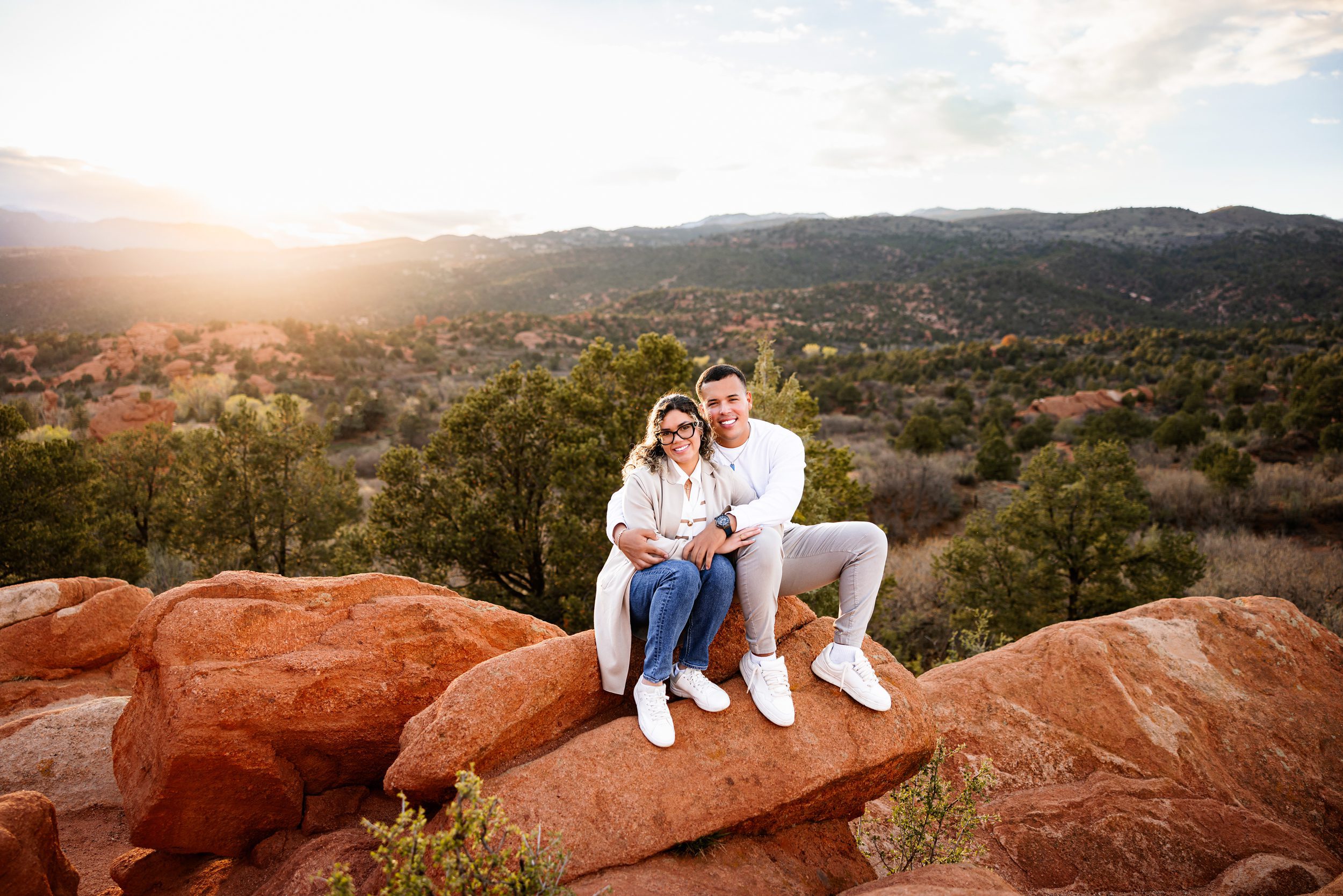 Couple sitting together on red rock formation with mountain views in Garden of the Gods proposal photos