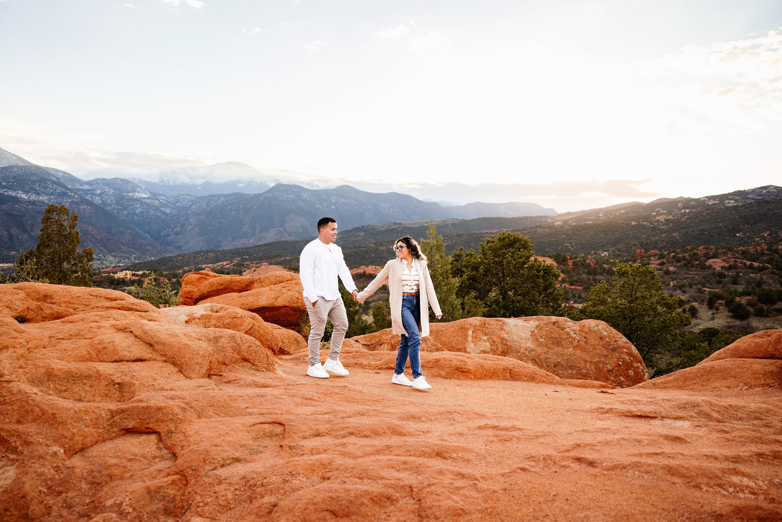 Couple walking hand in hand across red rocks with dramatic Colorado landscape