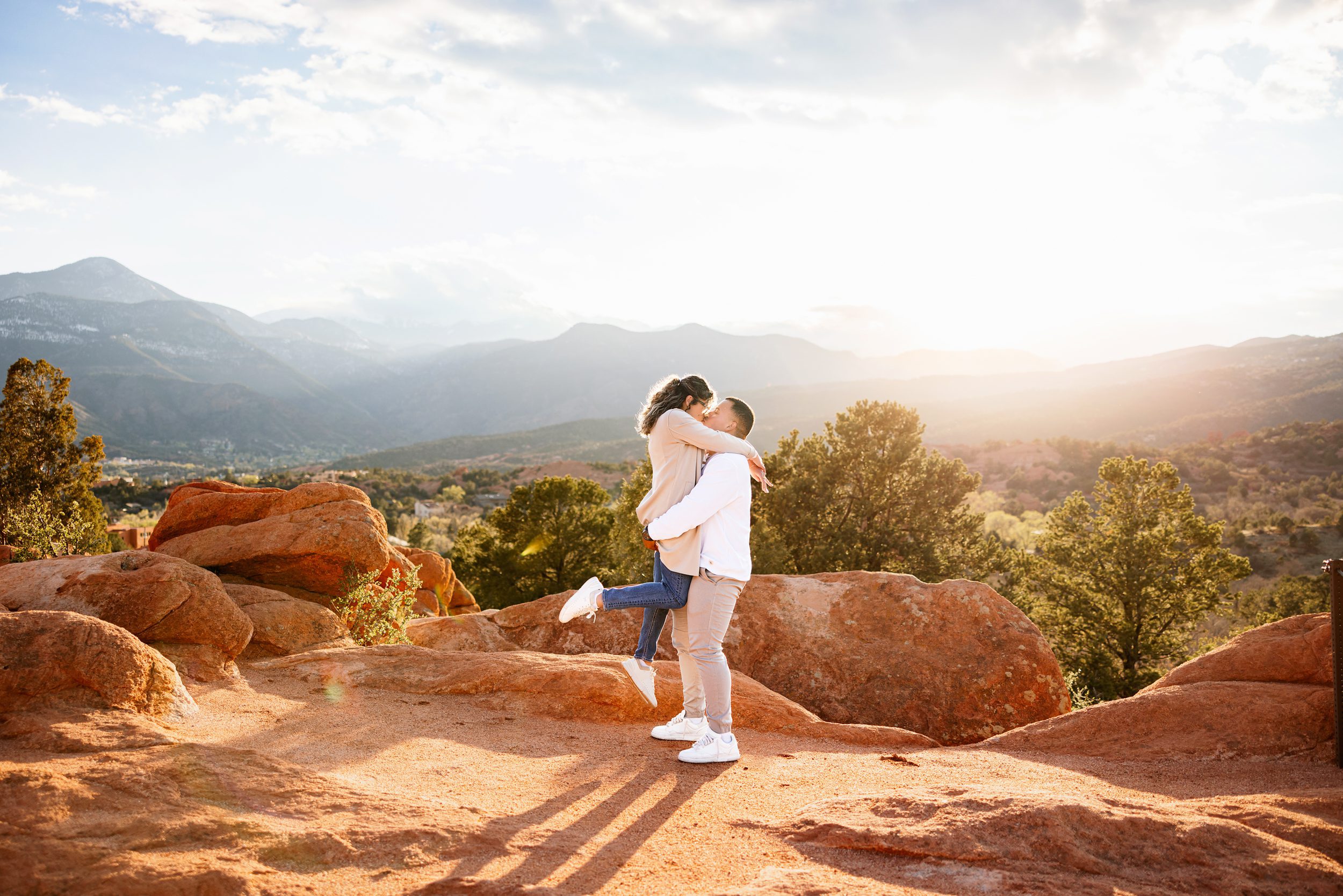 Couple kissing on red rocks with warm sunset light and scenic overlook