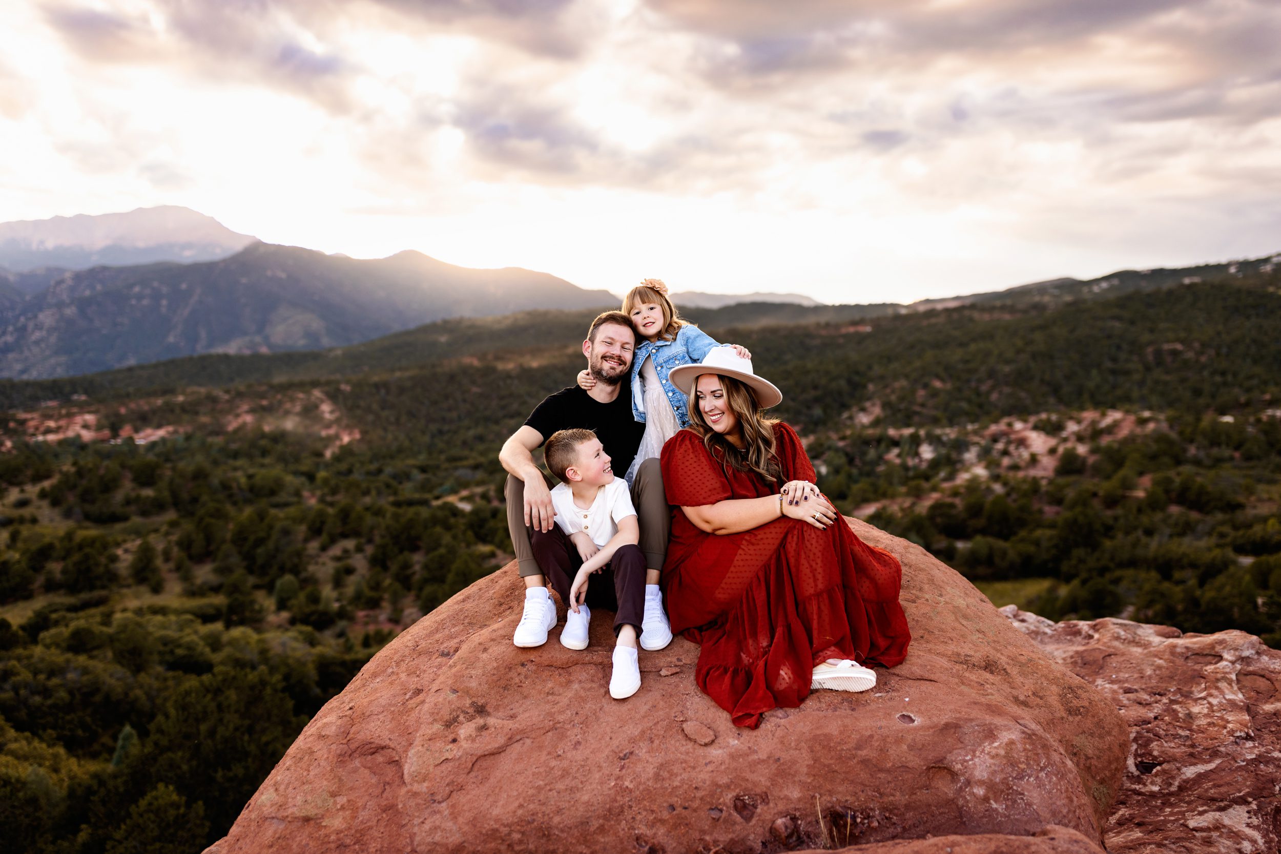 Garden of the Gods family photos of a family sitting together on a red rock overlook with mountain views at sunset