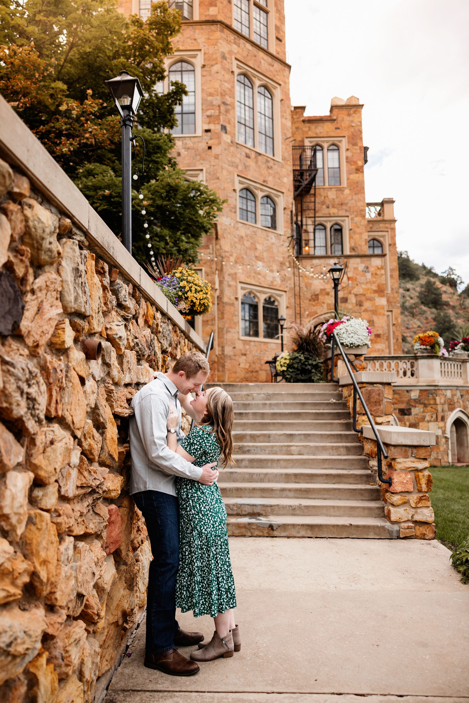 Glen Eyrie Couples Photos in Colorado Springs capturing a couple embracing by a stone wall and staircase with warm evening light