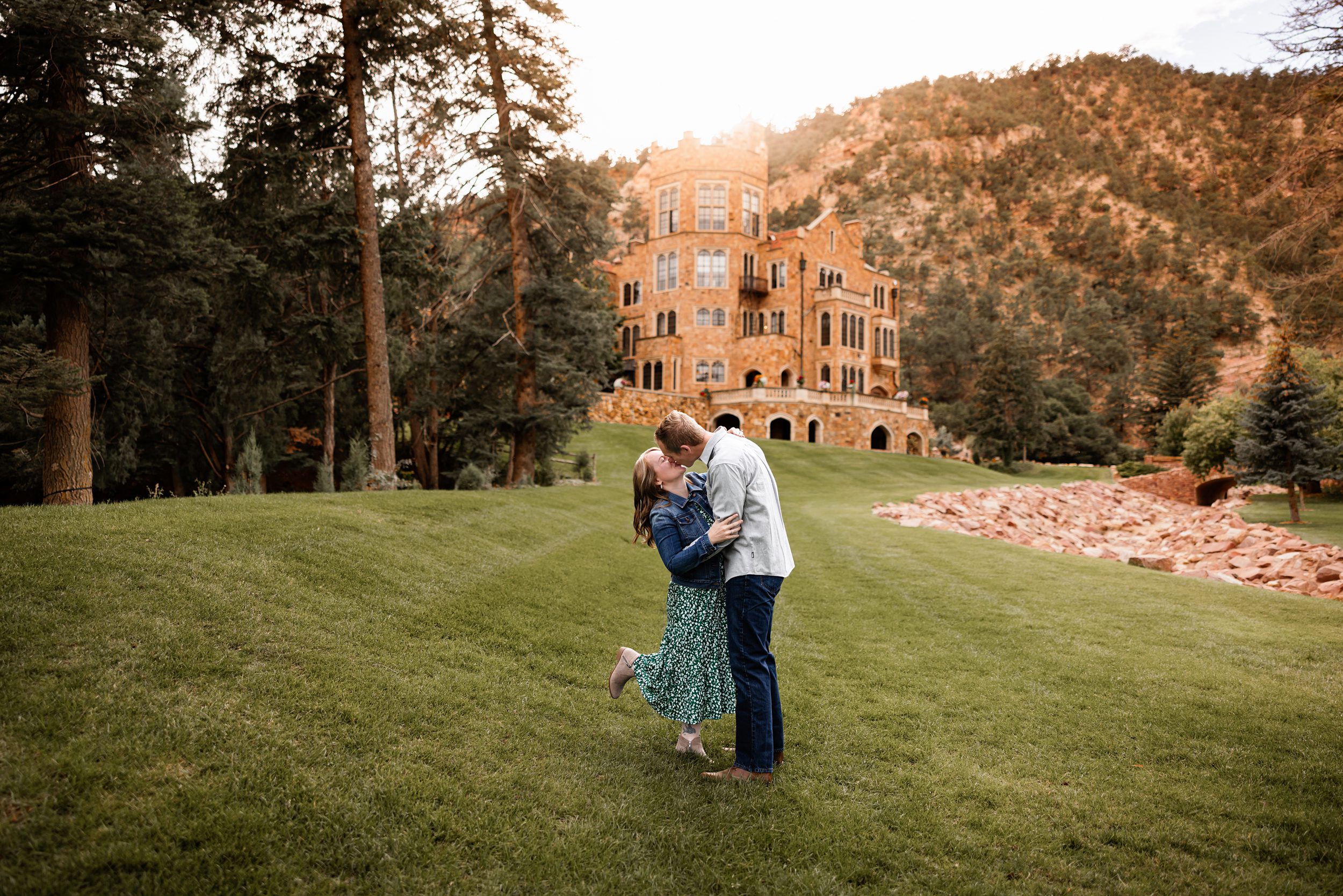 Glen Eyrie Couples Photos in Colorado Springs of a couple sharing a kiss on a grassy lawn with castle views behind them