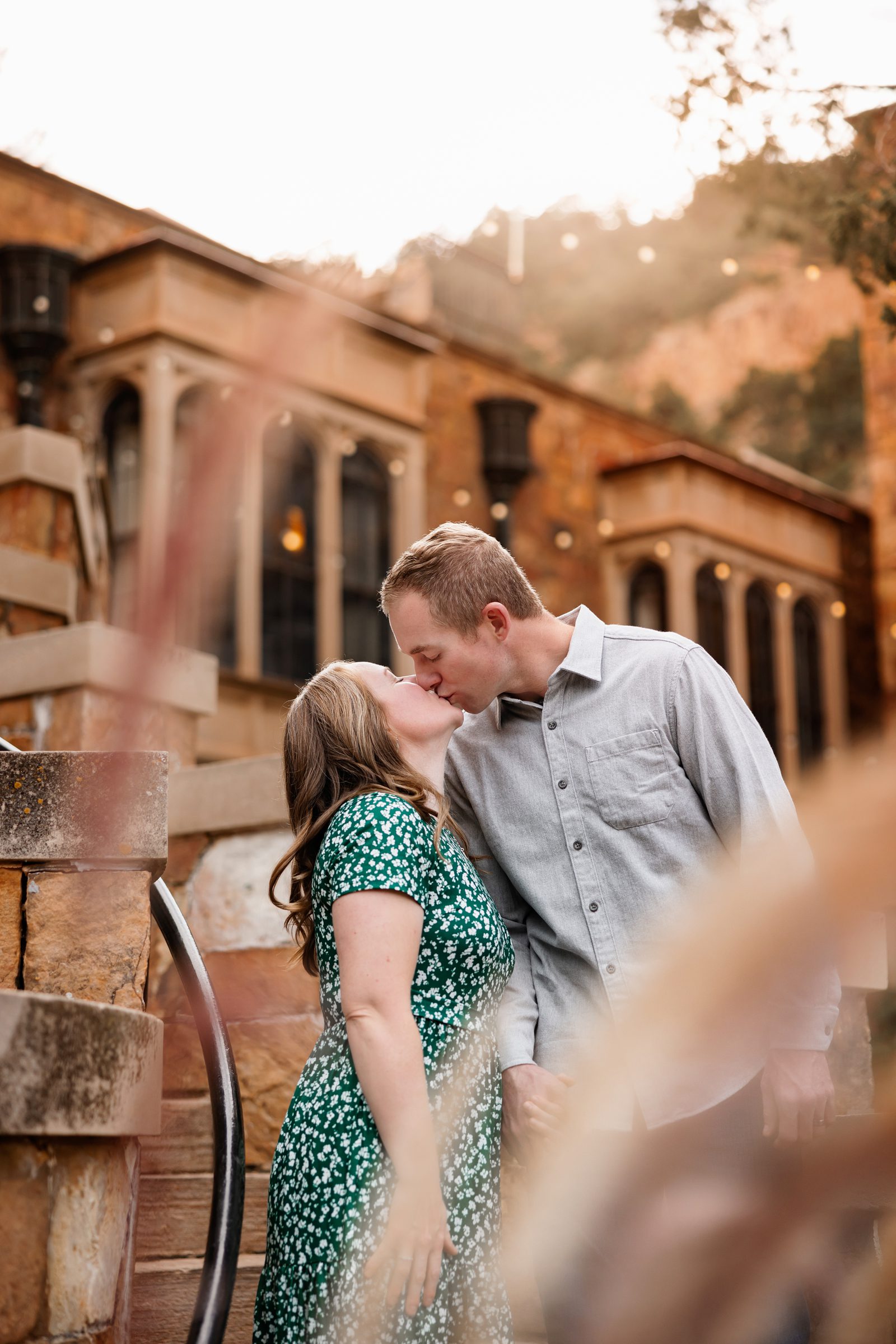 Close-up of couple kissing near Glen Eyrie castle with soft light, stone architecture, and romantic outdoor setting