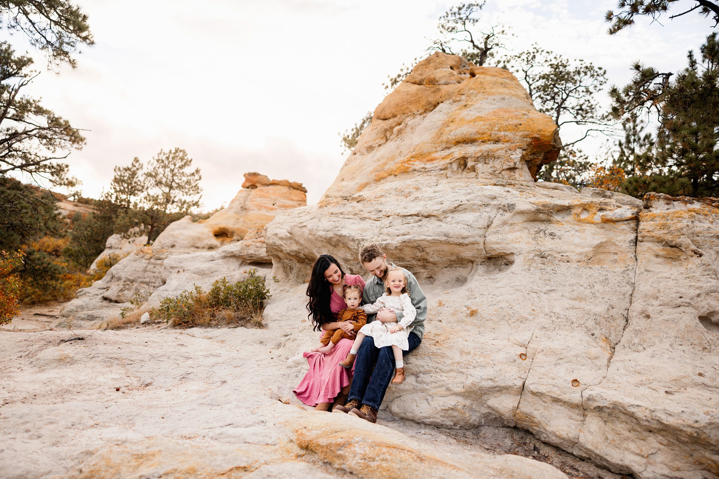 Mini session tips featuring a family of four sitting together on sandstone rocks with young kids smiling and cuddling