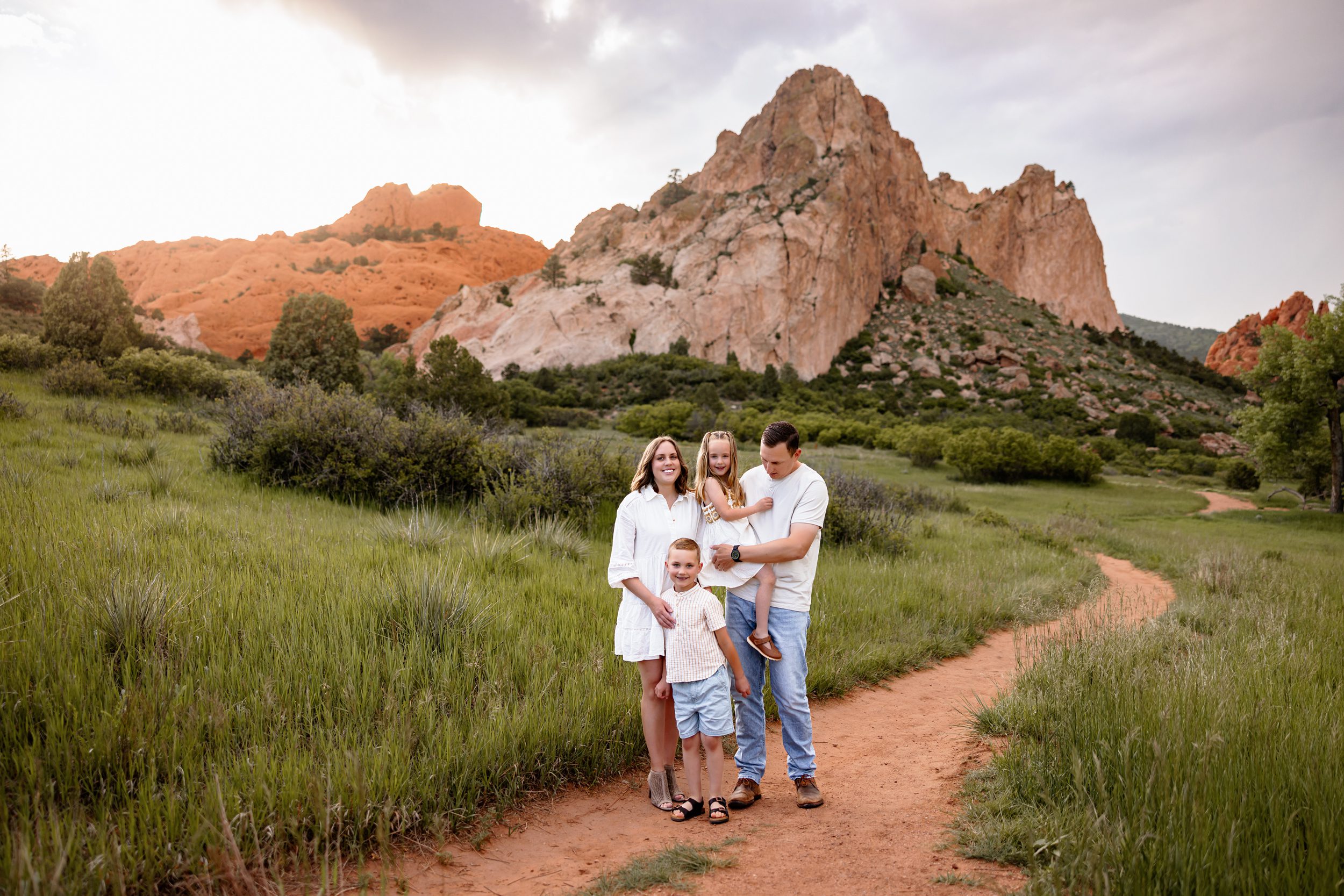Colorado Springs family photo with parents and two kids standing on a winding trail with mountain views