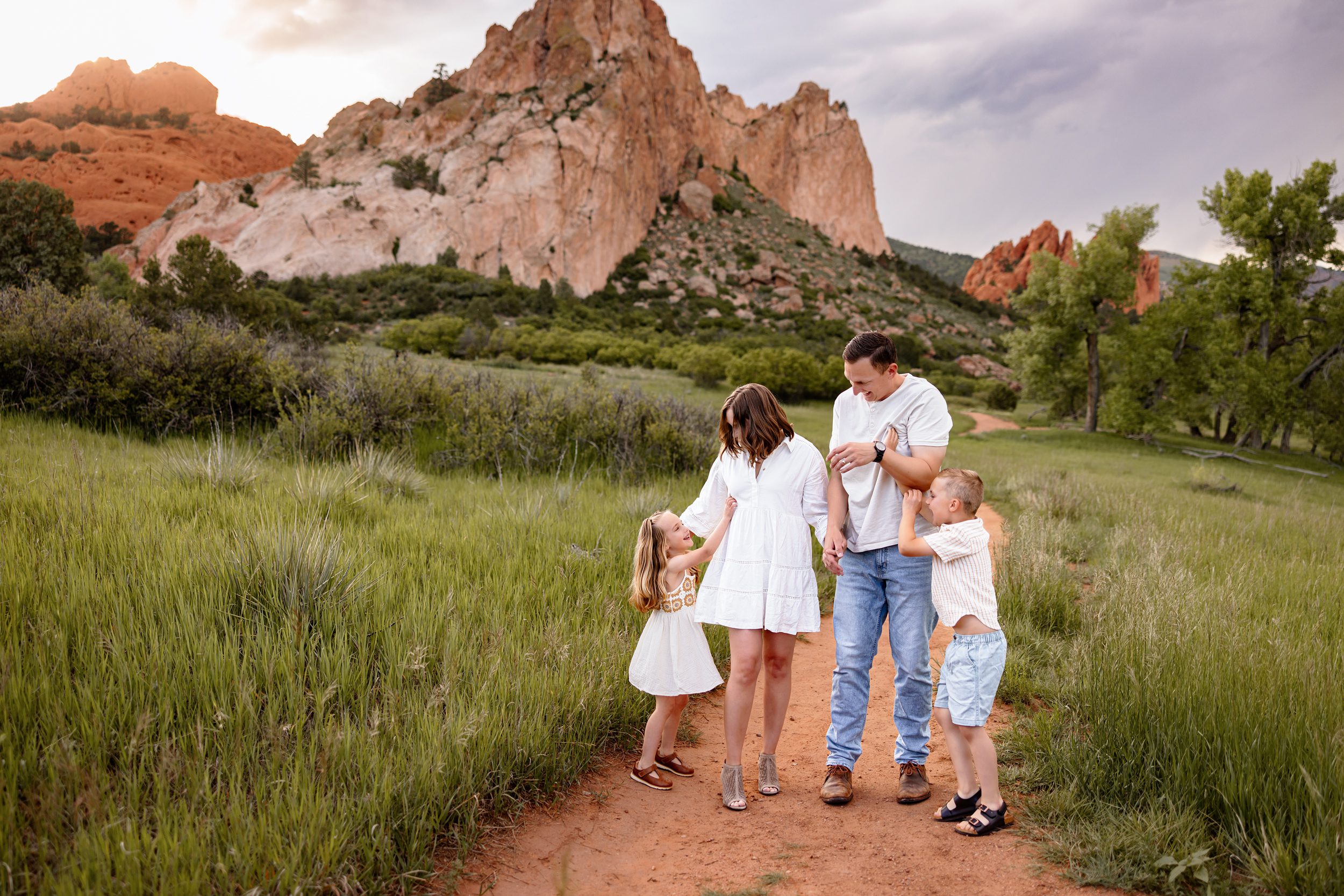 Family laughing and playing together on a trail at Garden of the Gods with glowing red rocks and soft evening light