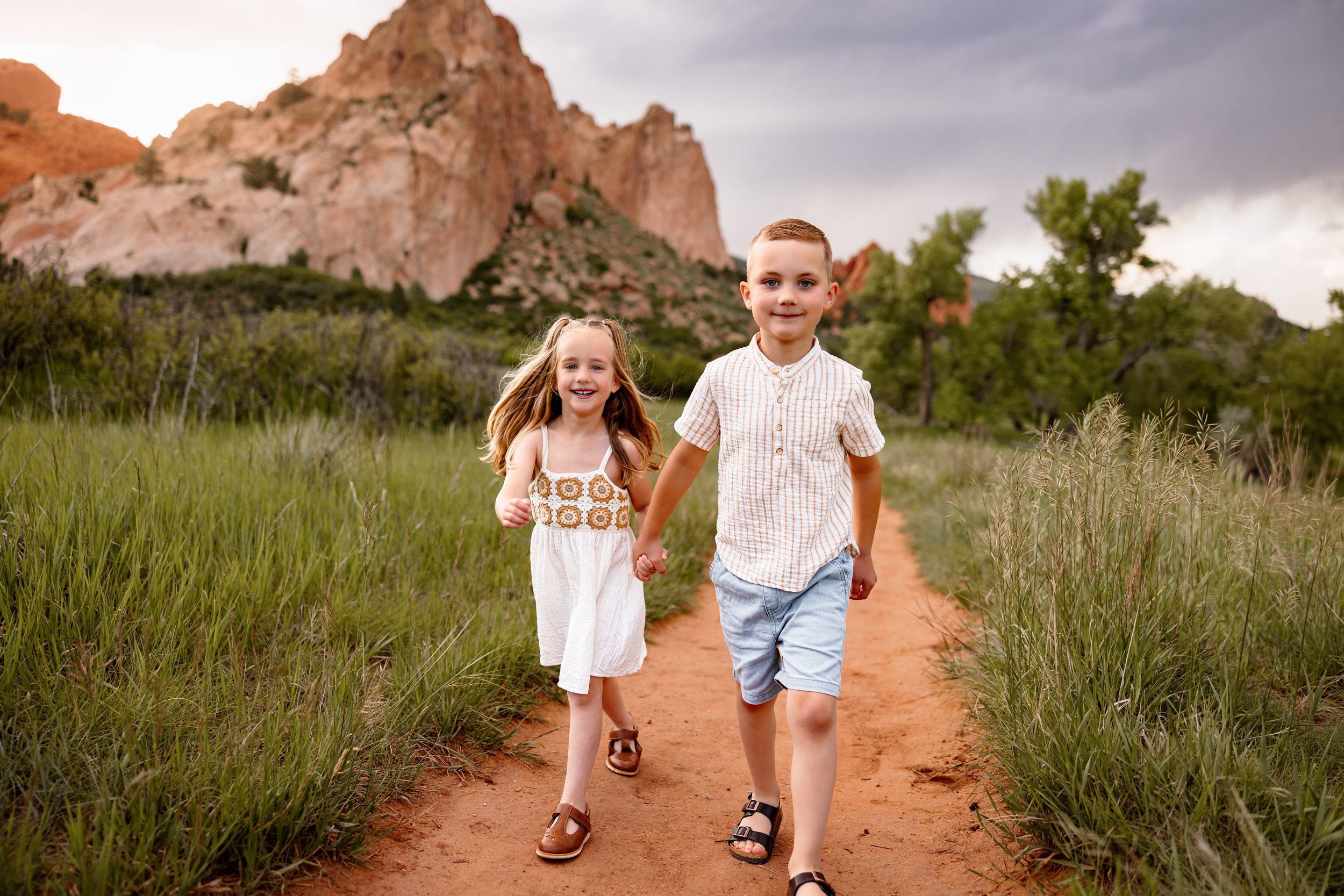 Siblings holding hands and walking toward the camera during a golden hour Colorado photo session