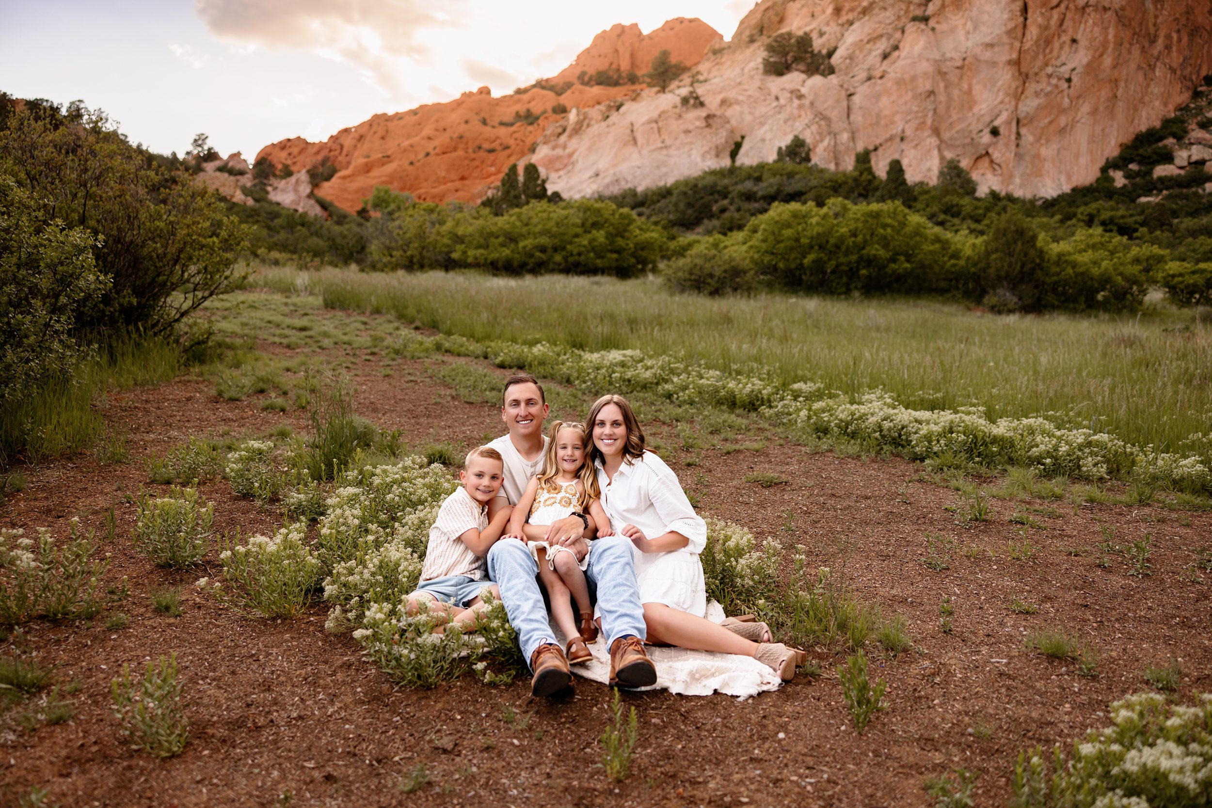 Family sitting together on the ground surrounded by wildflowers with mountain views behind them