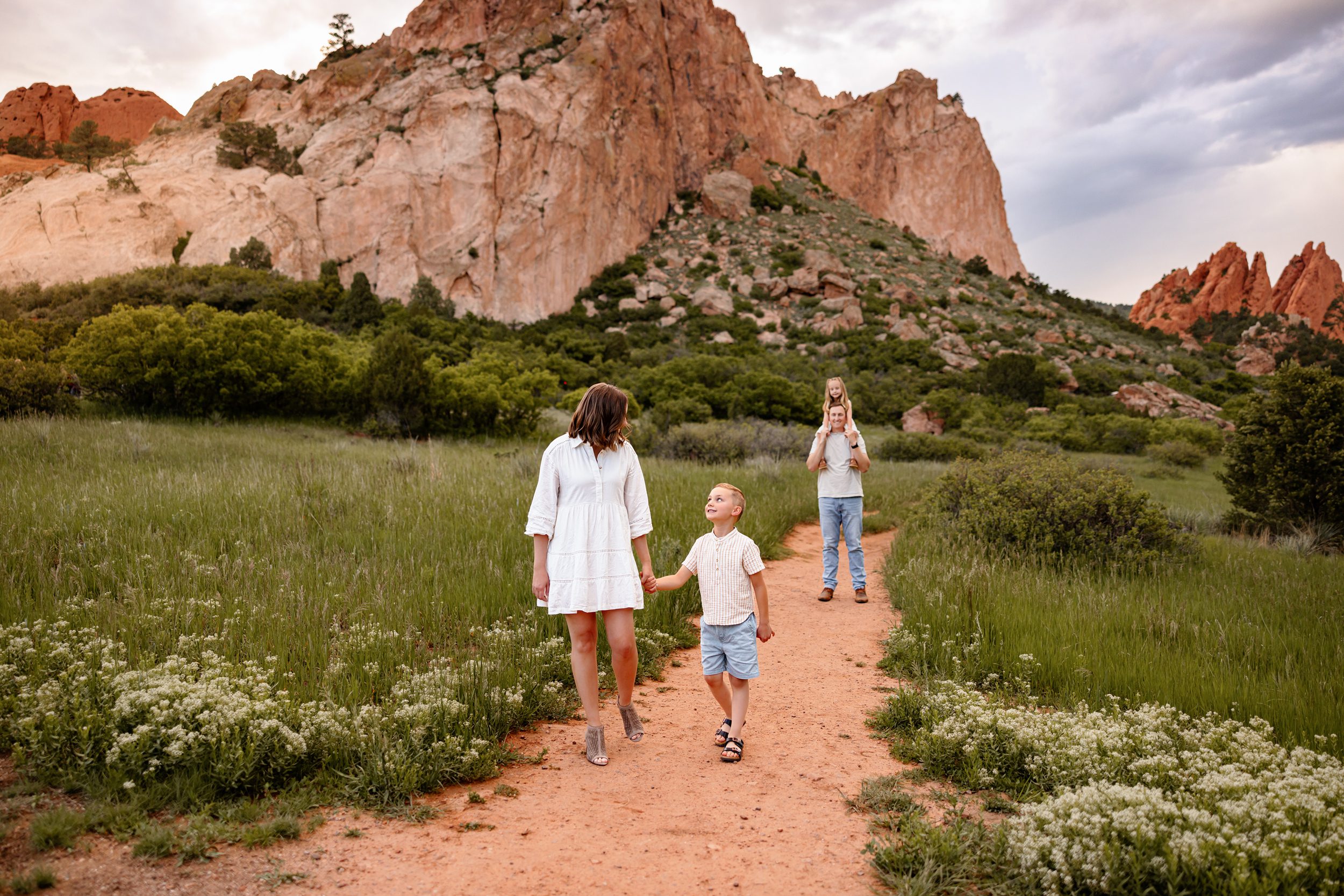 Mom and son walking hand in hand on a trail while dad carries daughter in the distance