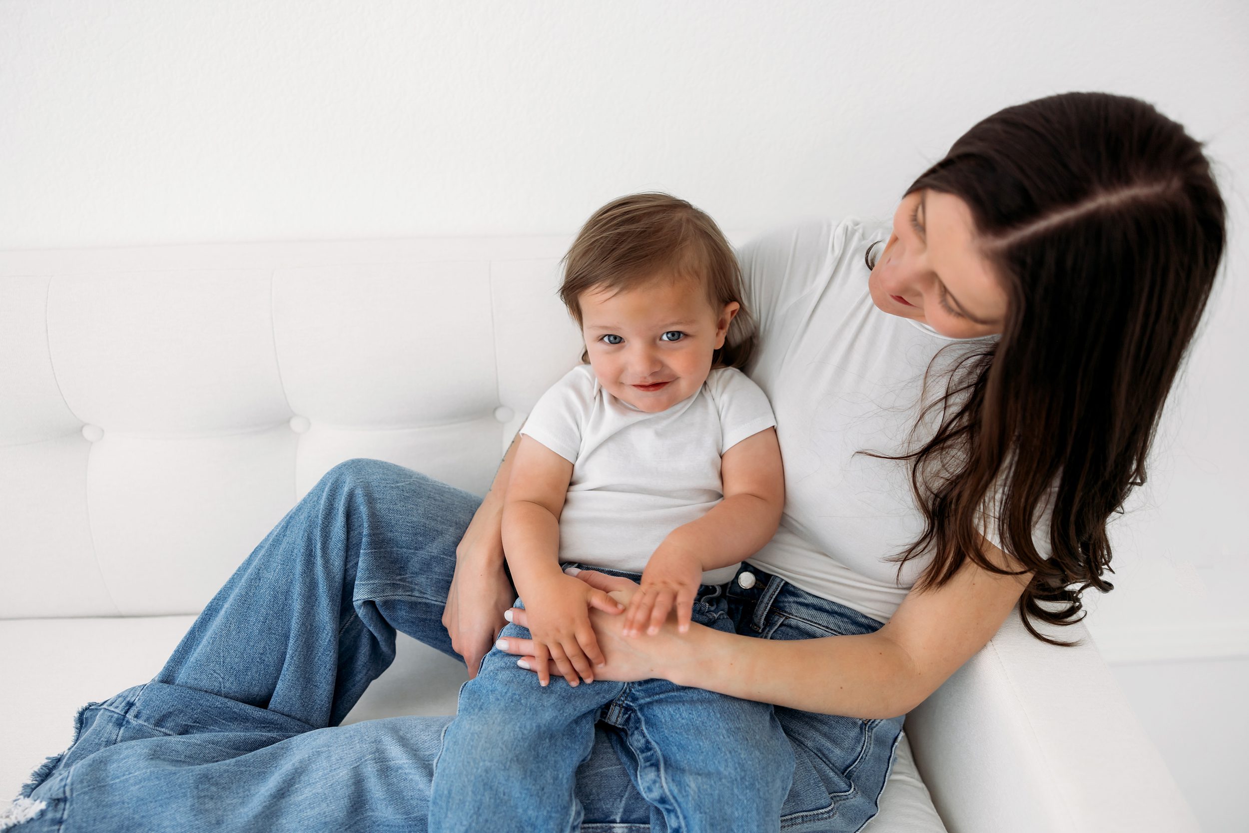 Mom and toddler cuddling on a white couch in a light-filled studio