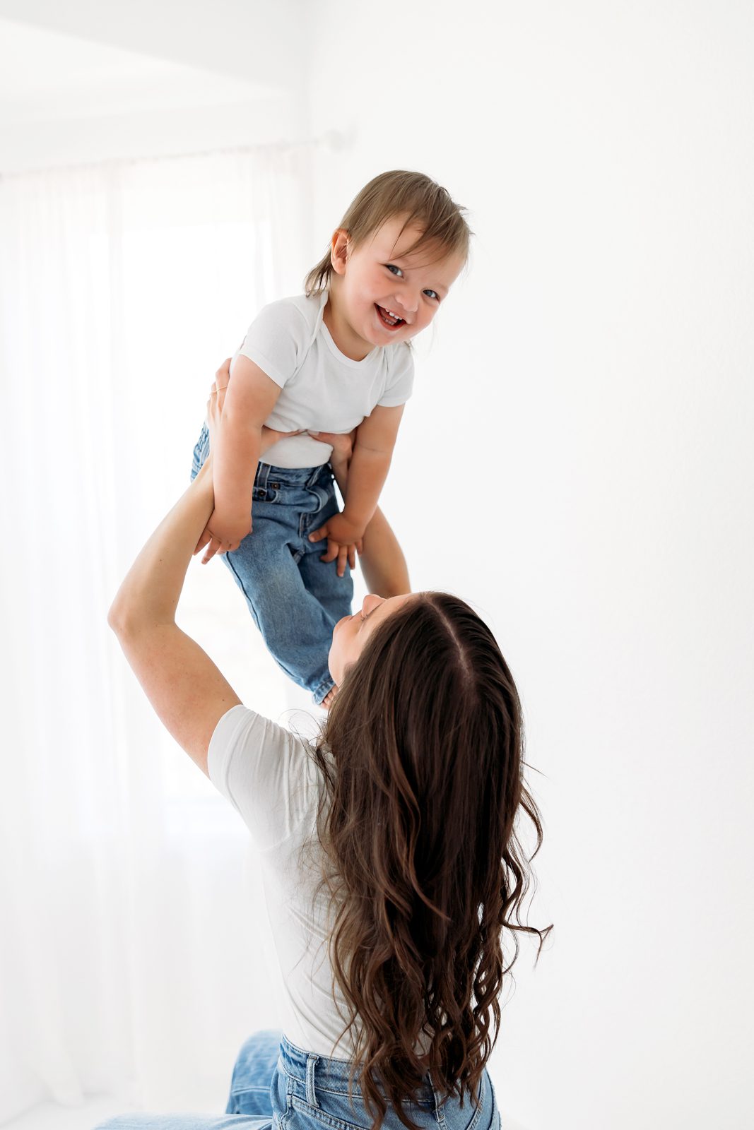 Studio Motherhood Photos in Colorado Springs with a mom lifting her toddler in a bright white studio