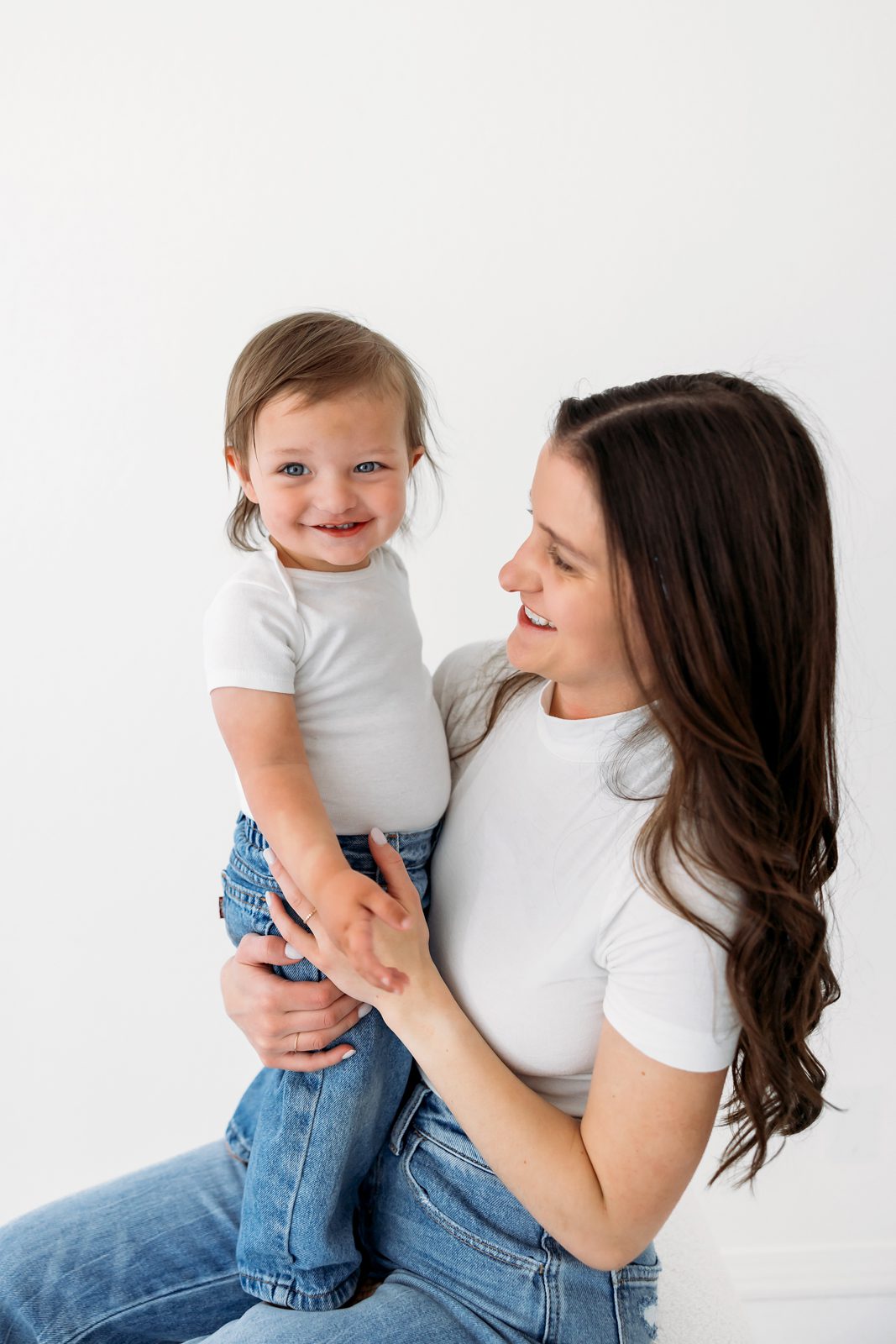 Smiling toddler held by mom during a cozy studio motherhood session
