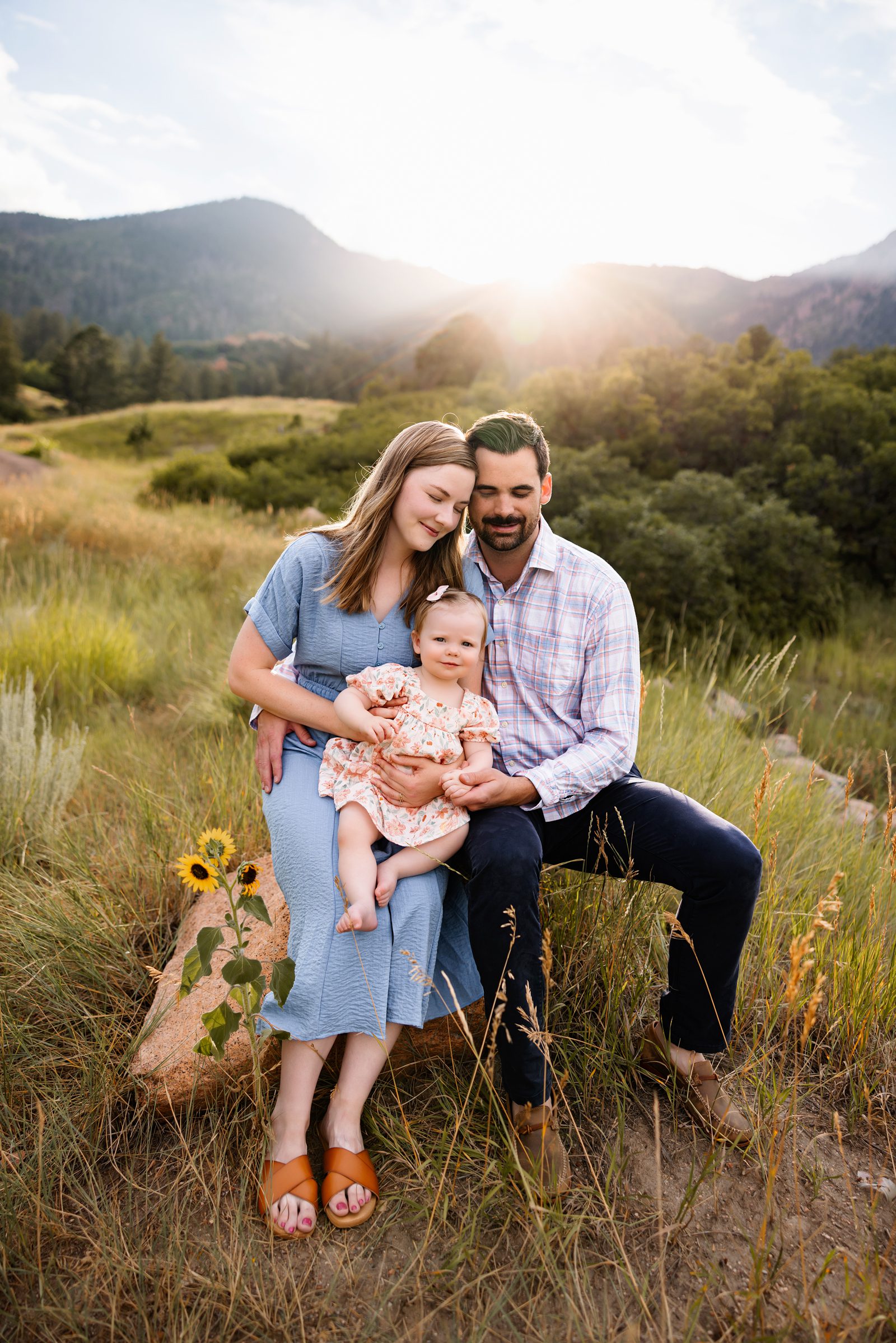 Parents and baby sharing a quiet moment together while sitting in tall grass at sunset