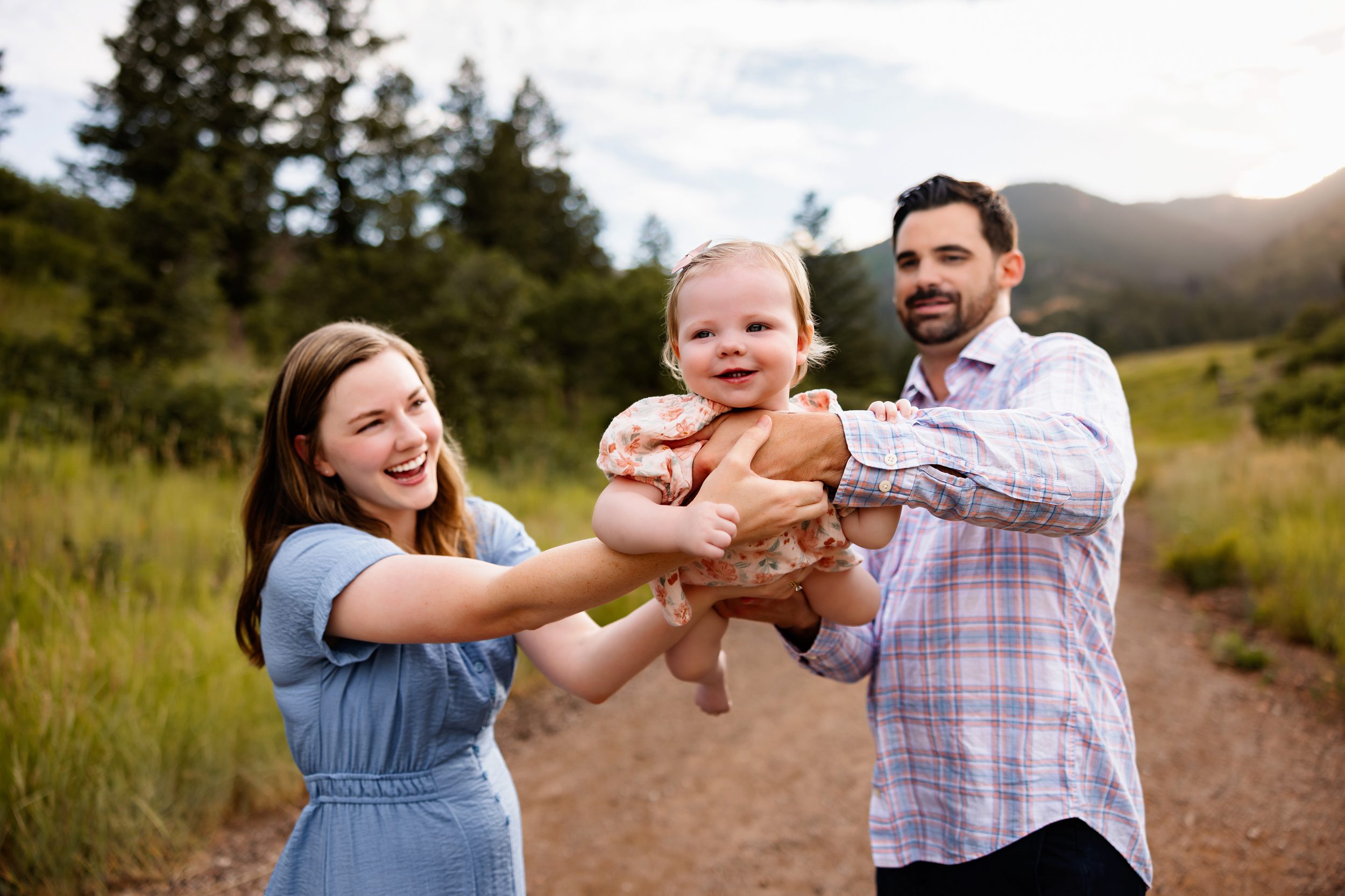 Playful family moment with parents lifting their baby girl in the air along a mountain path