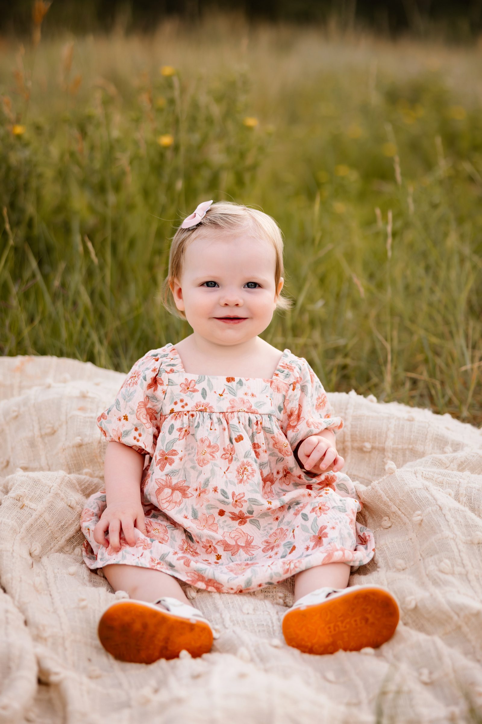 Baby girl sitting on a blanket in a grassy field during a warm summer evening