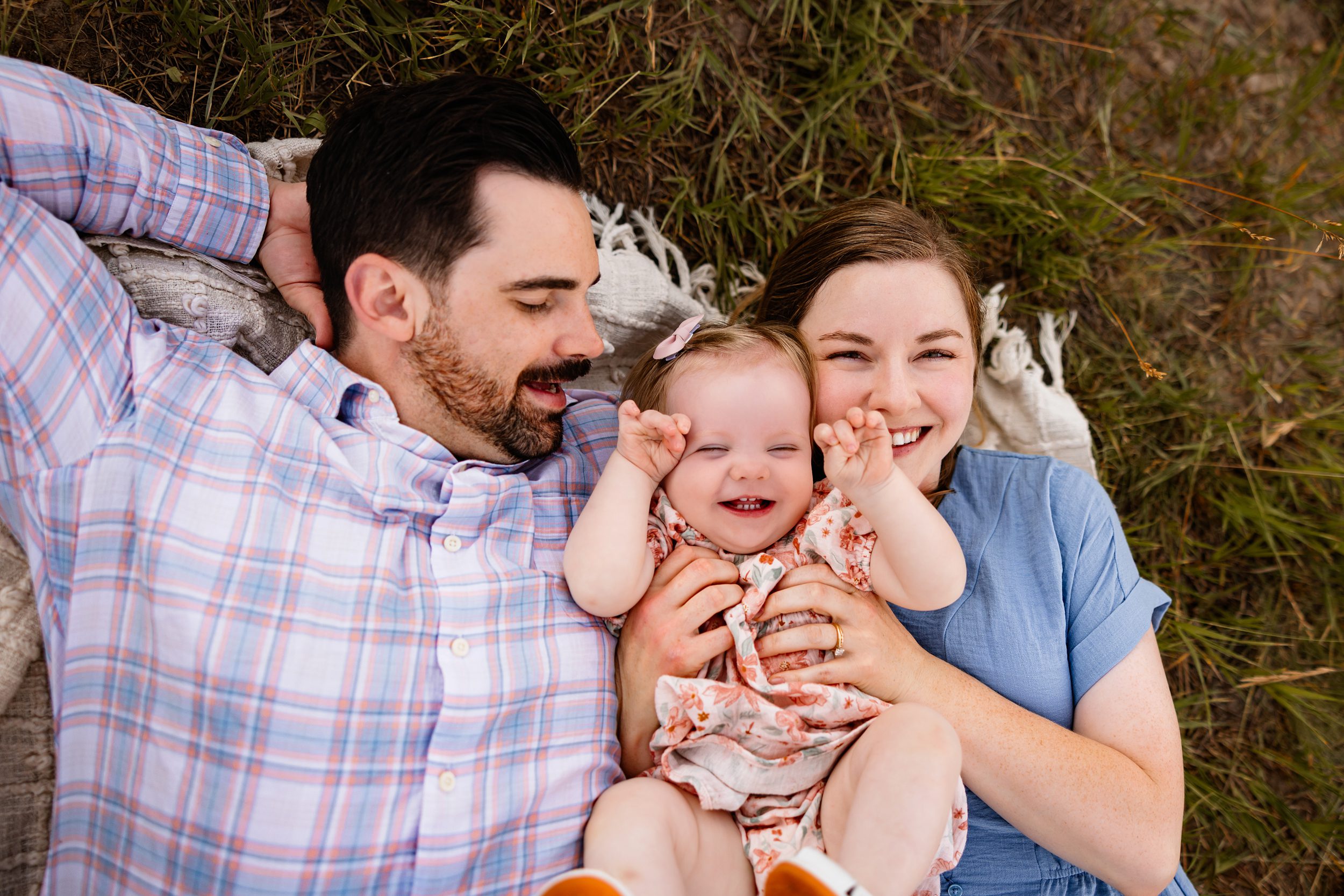 Family of three cuddling together in a grassy meadow with mountain views during golden hour